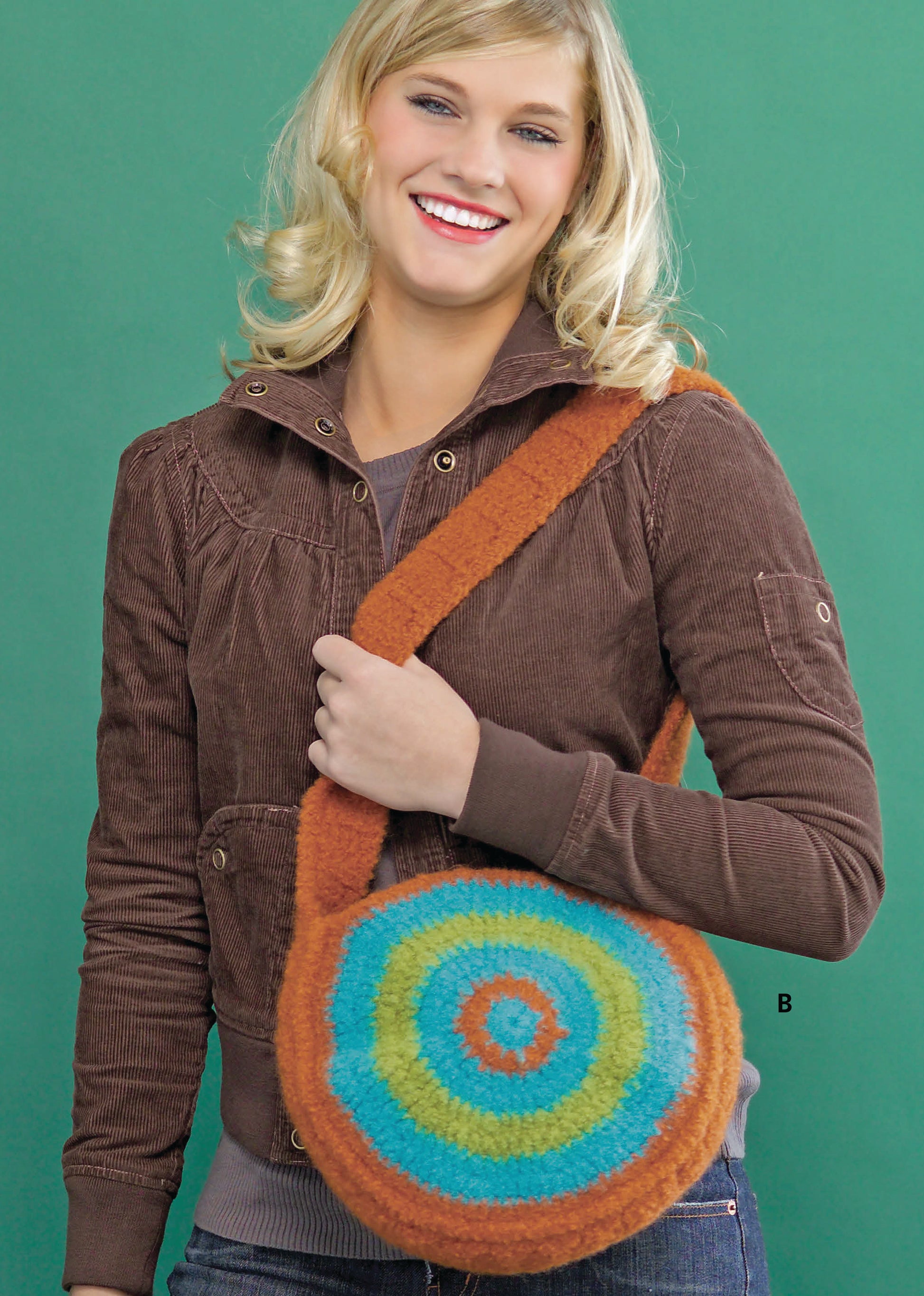 A smiling person holds a round, colorful felted bag with blue, green, yellow, and orange concentric circles—crafted using Leisure Arts' "I Can't Believe I'm Crocheting!" guide—perfect for crochet beginners.