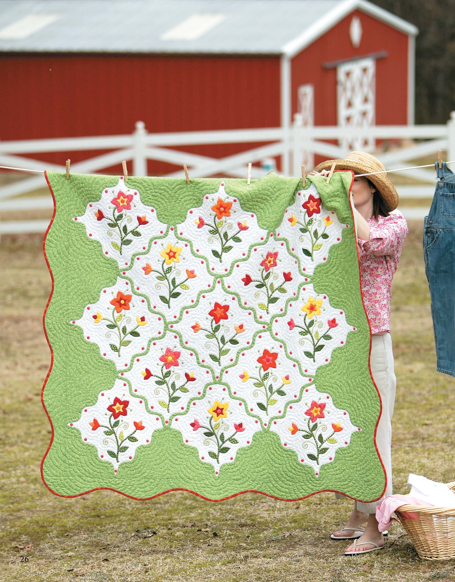 Outdoors near a red barn and white fence, someone displays the Garden of Appliqué Digital Download quilt by Leisure Arts. The quilt features green, nature-inspired and colorful floral patterns; jeans on a line add to this charming scene.