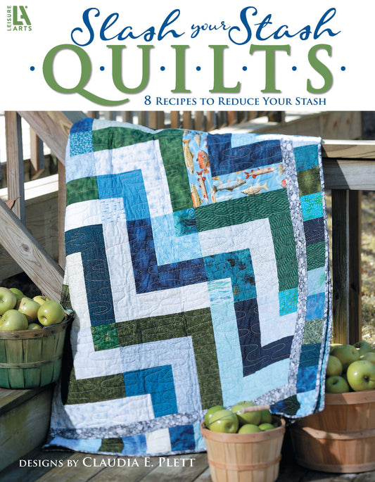 A blue, green, and white zigzag quilt lies on wooden steps near baskets of green apples. The book, Slash Your Stash Quilts by Leisure Arts, offers 8 stash-busting quilt patterns with fast piecing techniques.