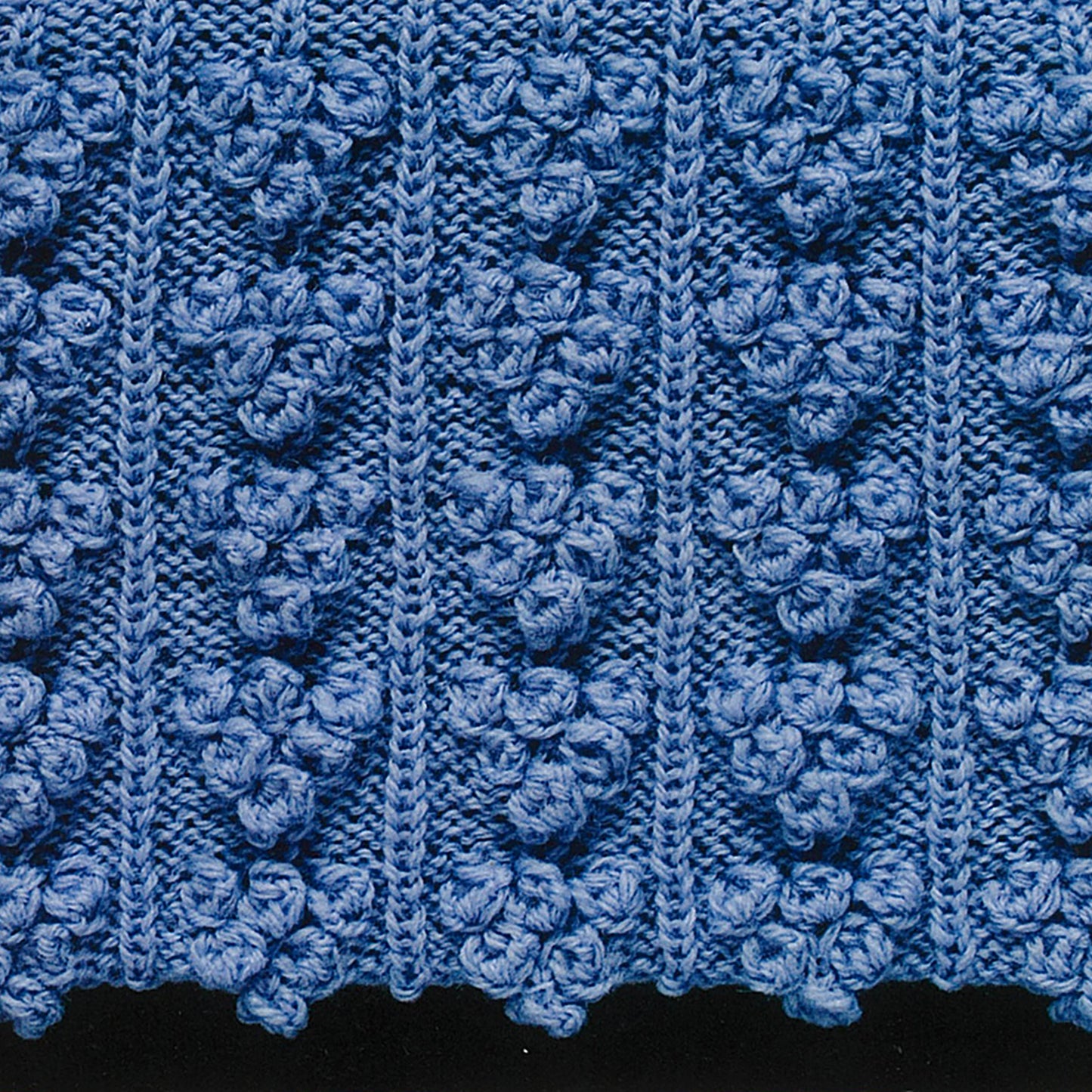Close-up of a blue knit fabric showcasing a textured pattern with bobbles and wavy lines—ideal for experimenting with decorative stitches from 50 Fabulous Knit Stitches by Leisure Arts.