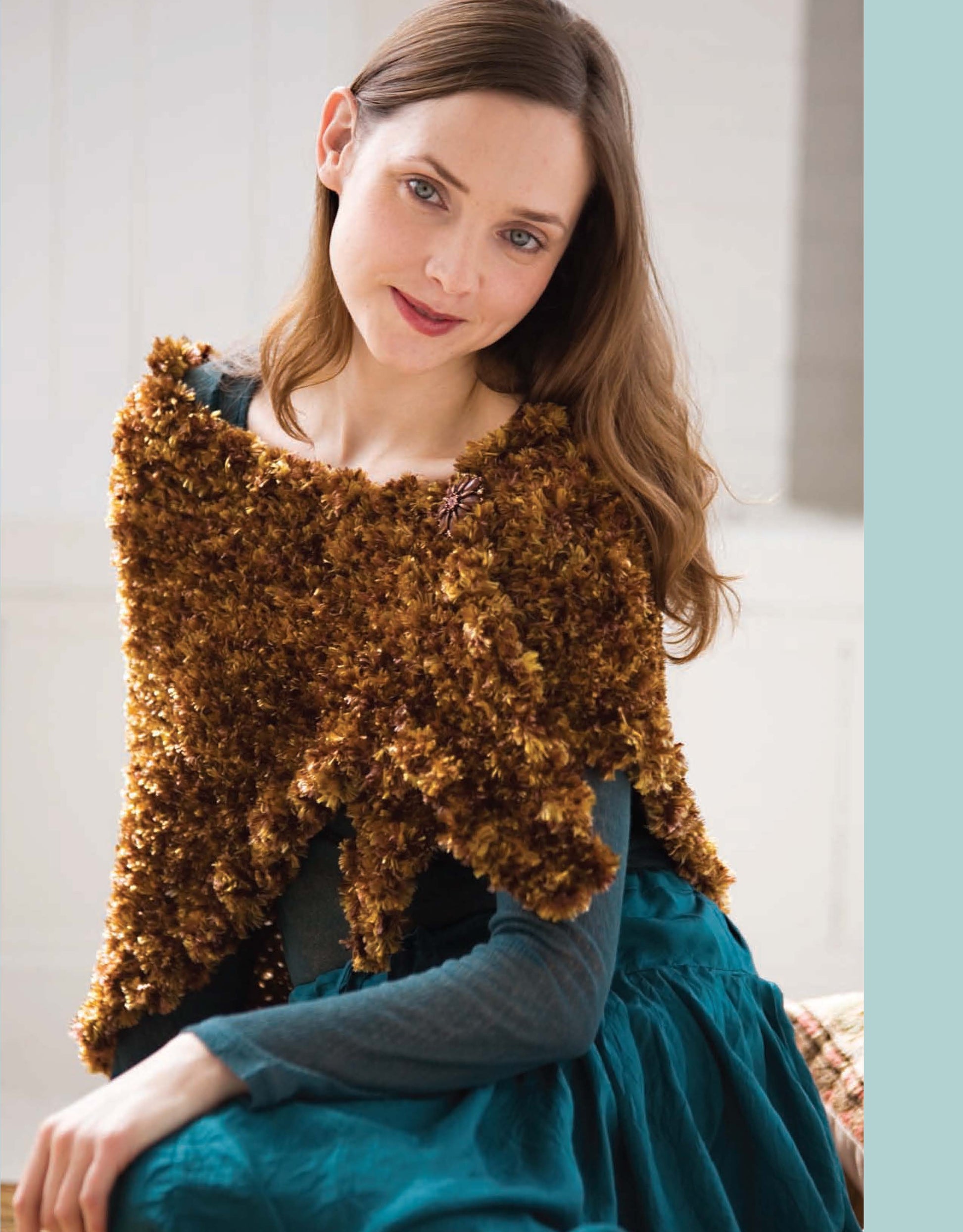 A woman with long brown hair, in a teal dress and textured brown crochet shawl, smiles softly at the camera—ready for a feature in Leisure Arts’ latest Romantic Looks Crochet edition.