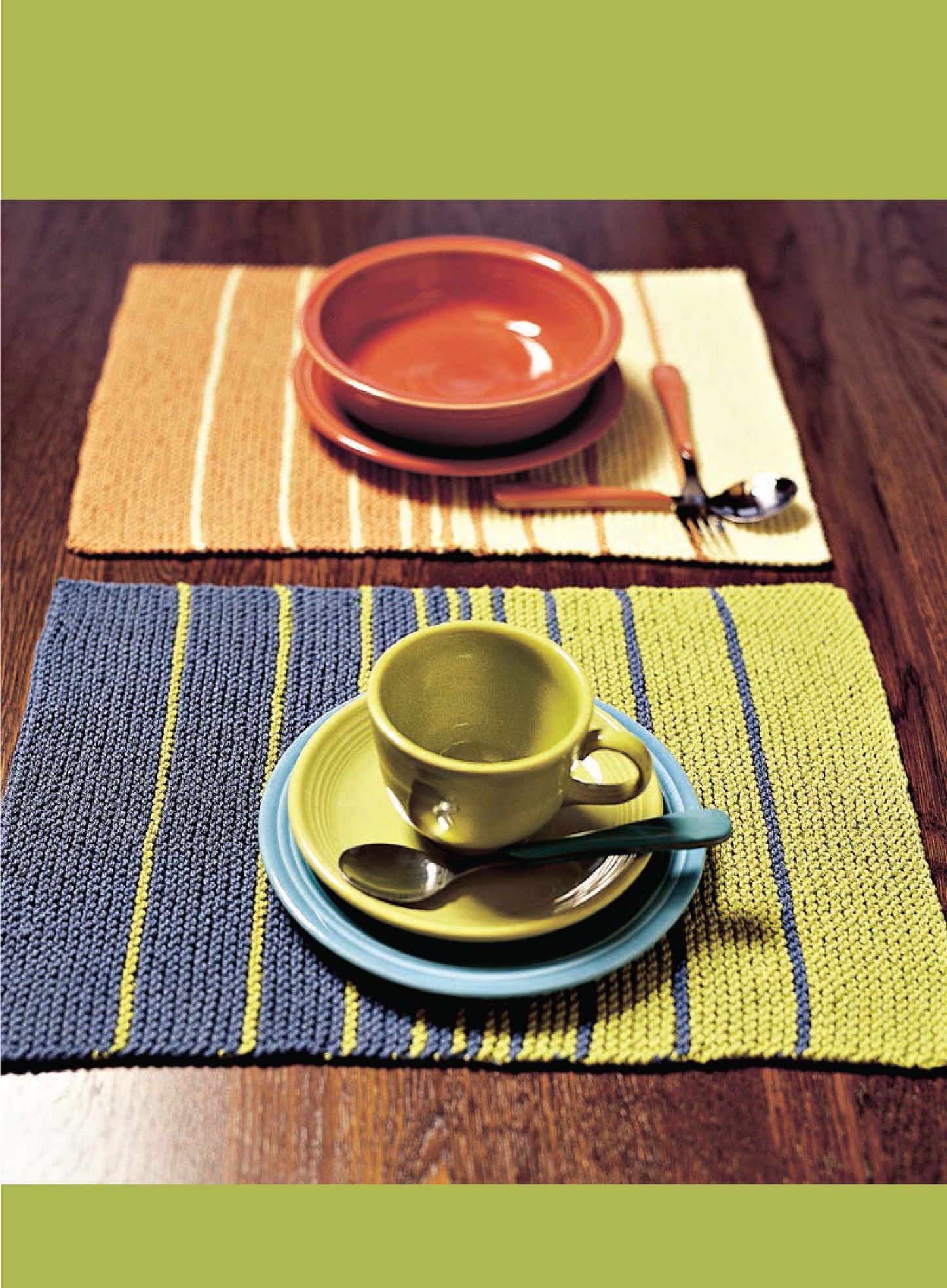 Two place settings on a wooden table; the front has a green cup and saucer with utensils, while the back features an orange bowl and plate. Styled with inspiration from Better Homes and Gardens 1-2-3 Knit by Leisure Arts.