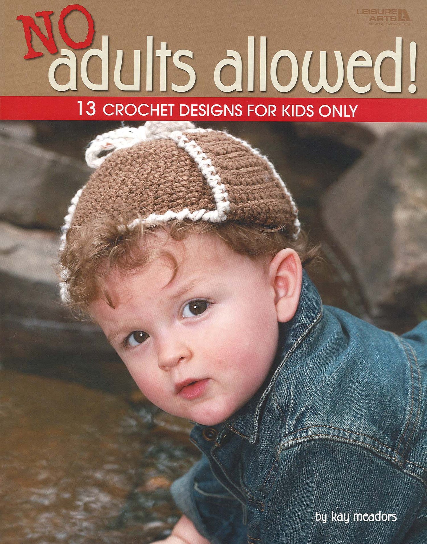 A curly-haired child in a brown crochet hat with white trim and blue jacket sits outdoors by rocks. The book cover reads: No Adults Allowed! Digital Download by Leisure Arts, featuring 13 crochet designs for kids only.