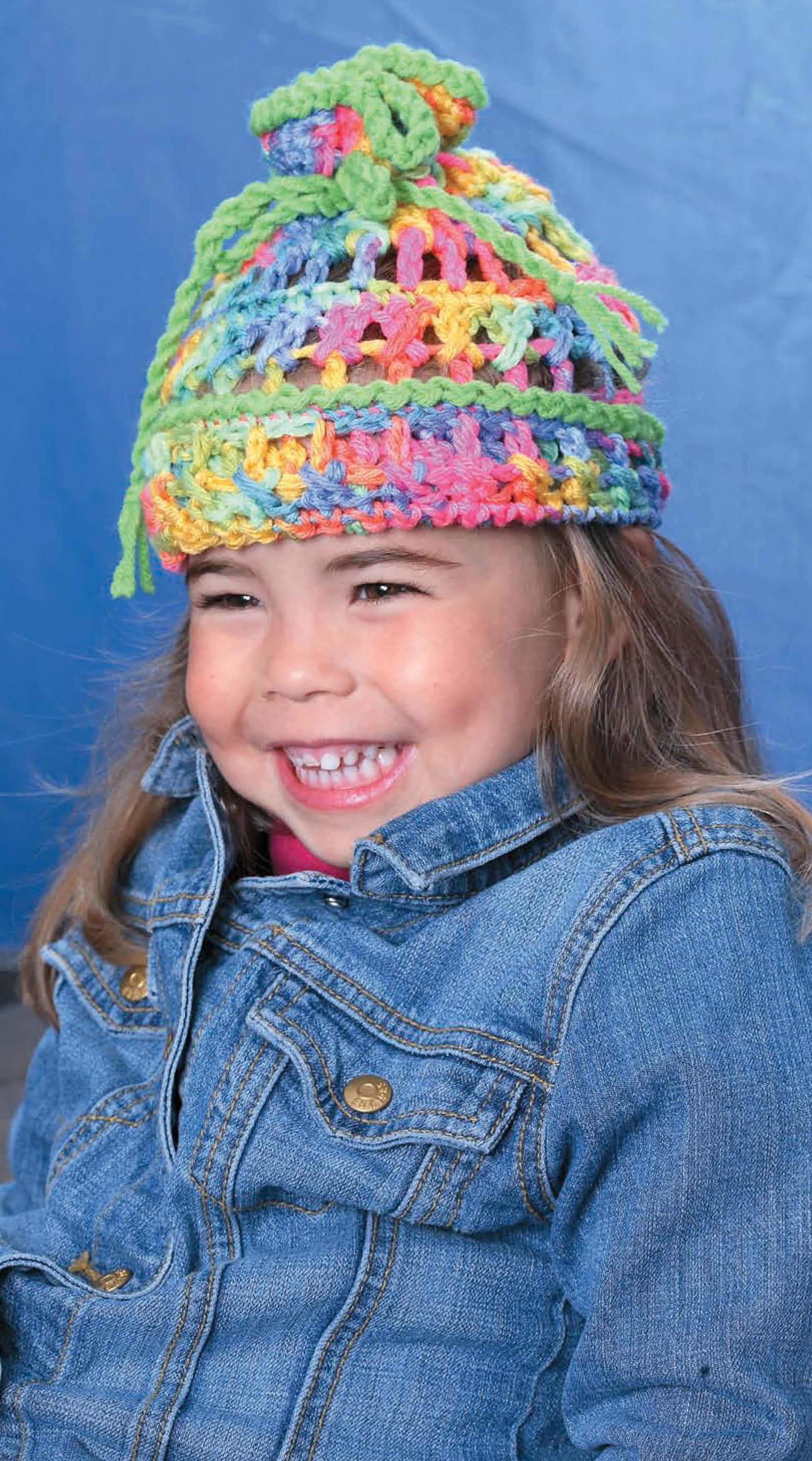 A young child with long hair smiles joyfully, sporting the "No Adults Allowed! Digital Download" by Leisure Arts, paired with a denim jacket against a plain blue background.