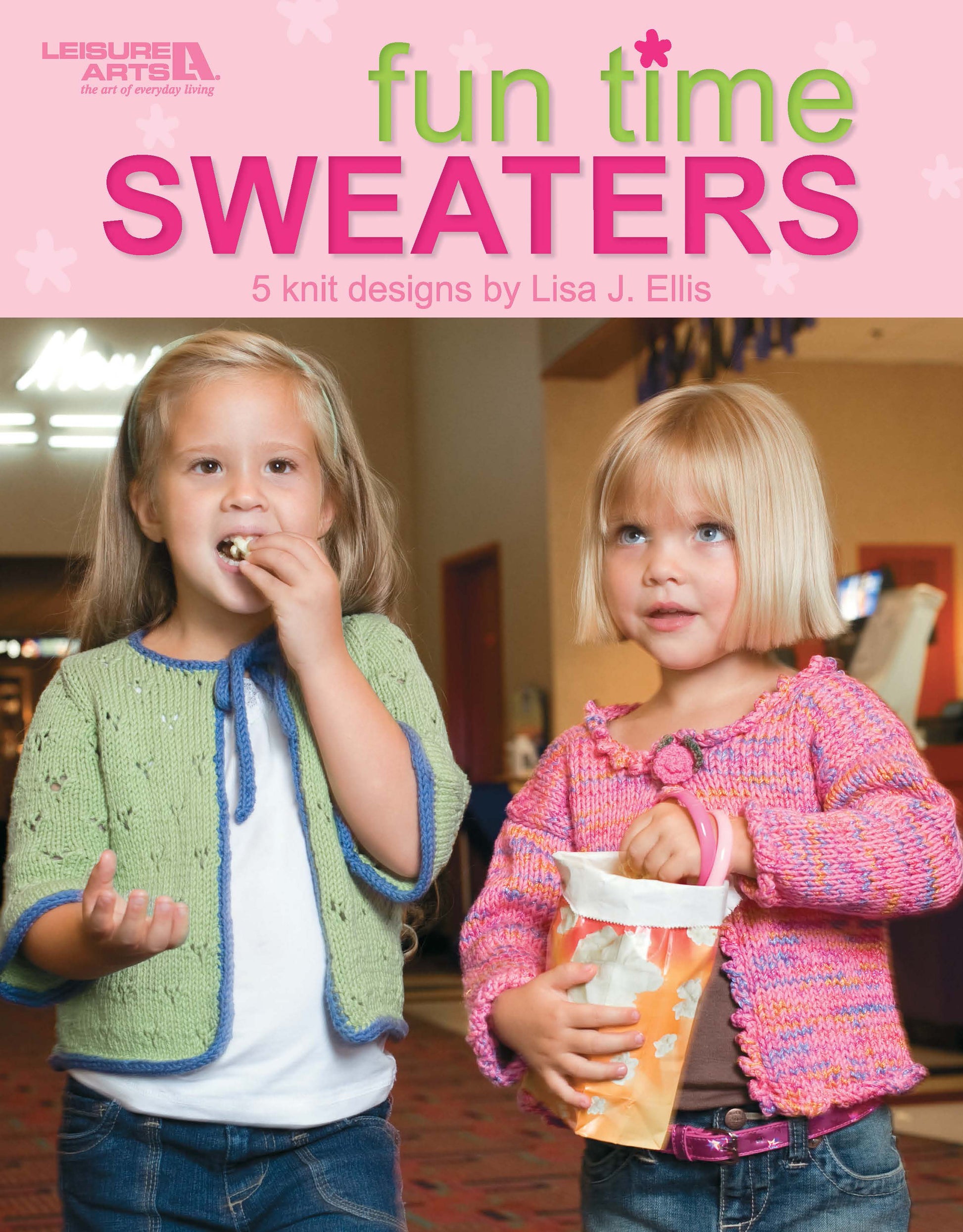 Two young girls stand indoors, eating popcorn. One wears a green cardigan with blue trim, the other a pink pullover with purple trim. Above them: "Fun Time Sweaters" by Leisure Arts—5 knit designs by Lisa J. Ellis.