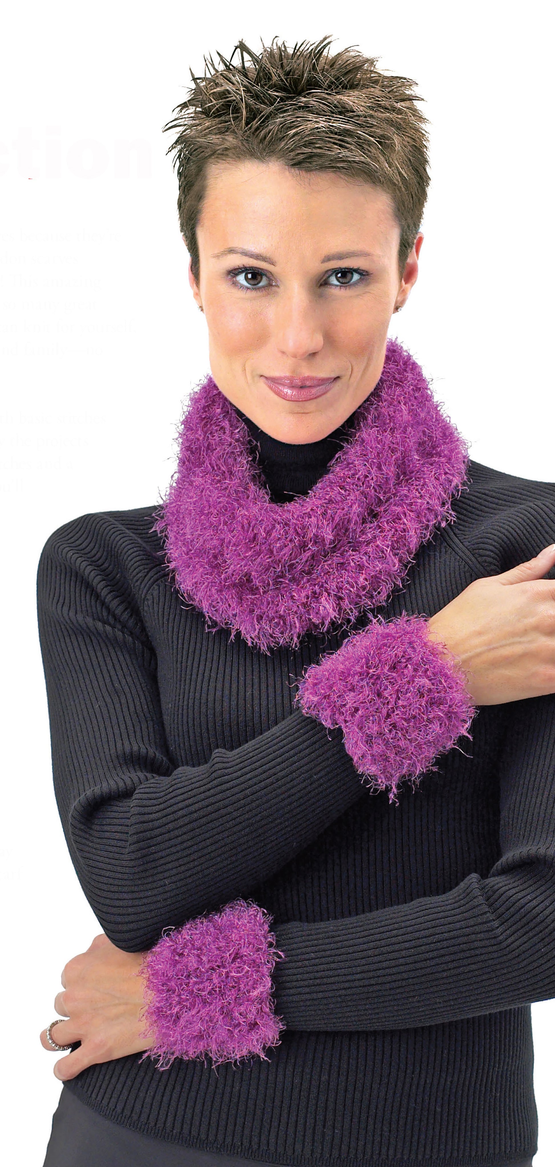 A person with short brown hair wears a black ribbed turtleneck sweater, a fuzzy purple cowl scarf, and matching wrist cuffs—perfect inspiration from Leisure Arts' Big Book of Knit Hats & Scarves for Everyone—smiling against a white background.