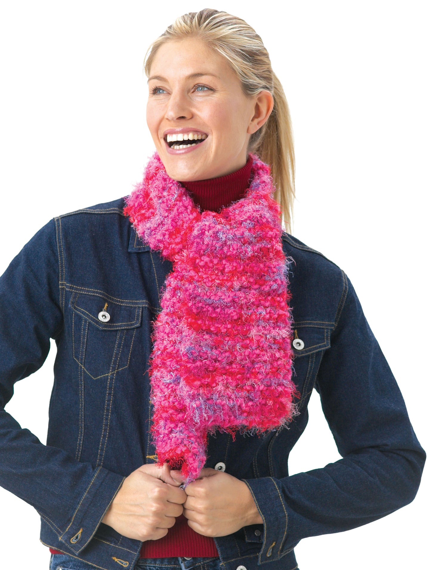 A smiling person in a red turtleneck, dark denim jacket, and fluffy pink scarf stands against a white background—perfect inspiration for projects from the Leisure Arts Big Book of Knit Hats & Scarves for Everyone.