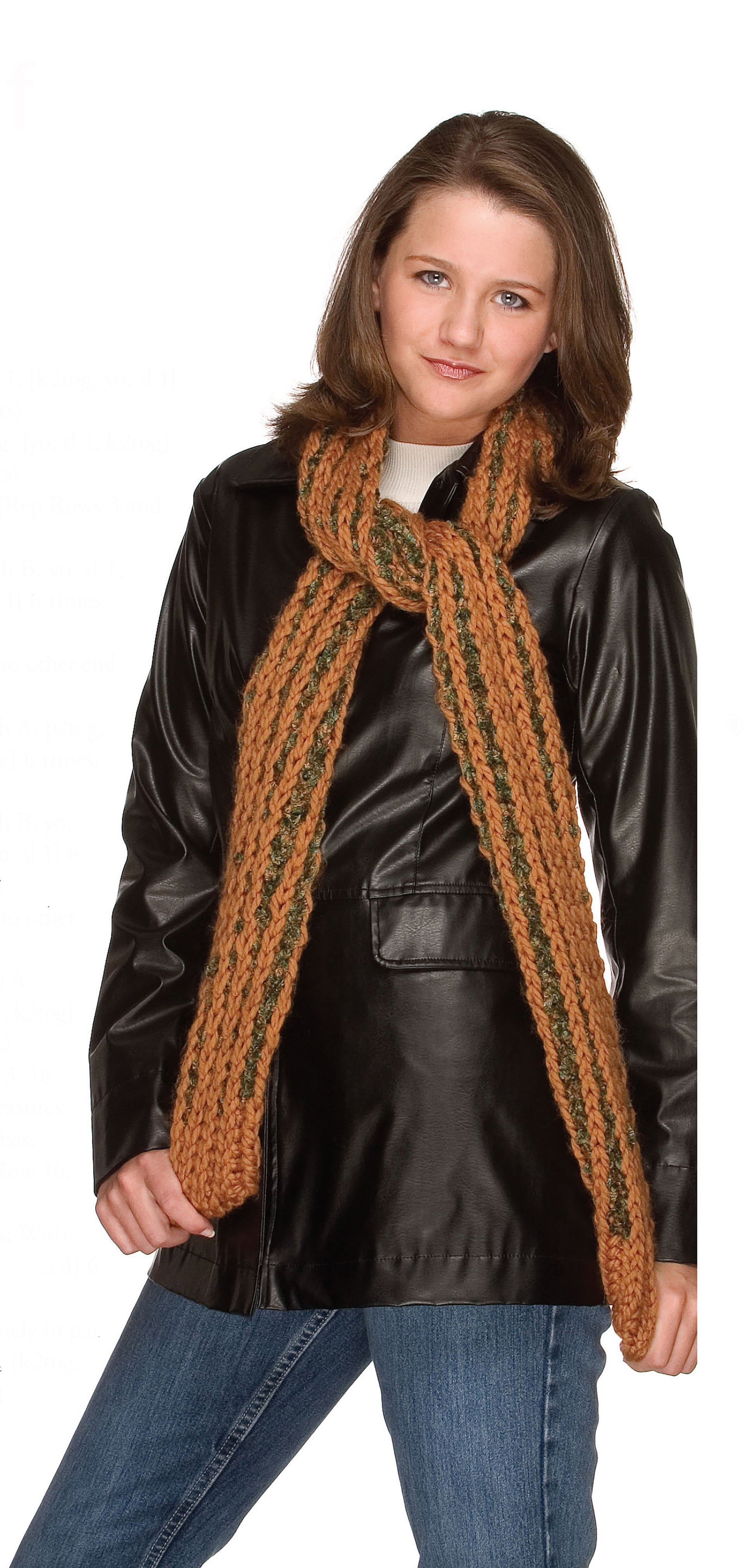 A young woman smiles slightly, wearing a black leather jacket, blue jeans, and a chunky orange and green scarf made from patterns in the "Big Book of Knit Hats & Scarves for Everyone" by Leisure Arts, standing against a white background.