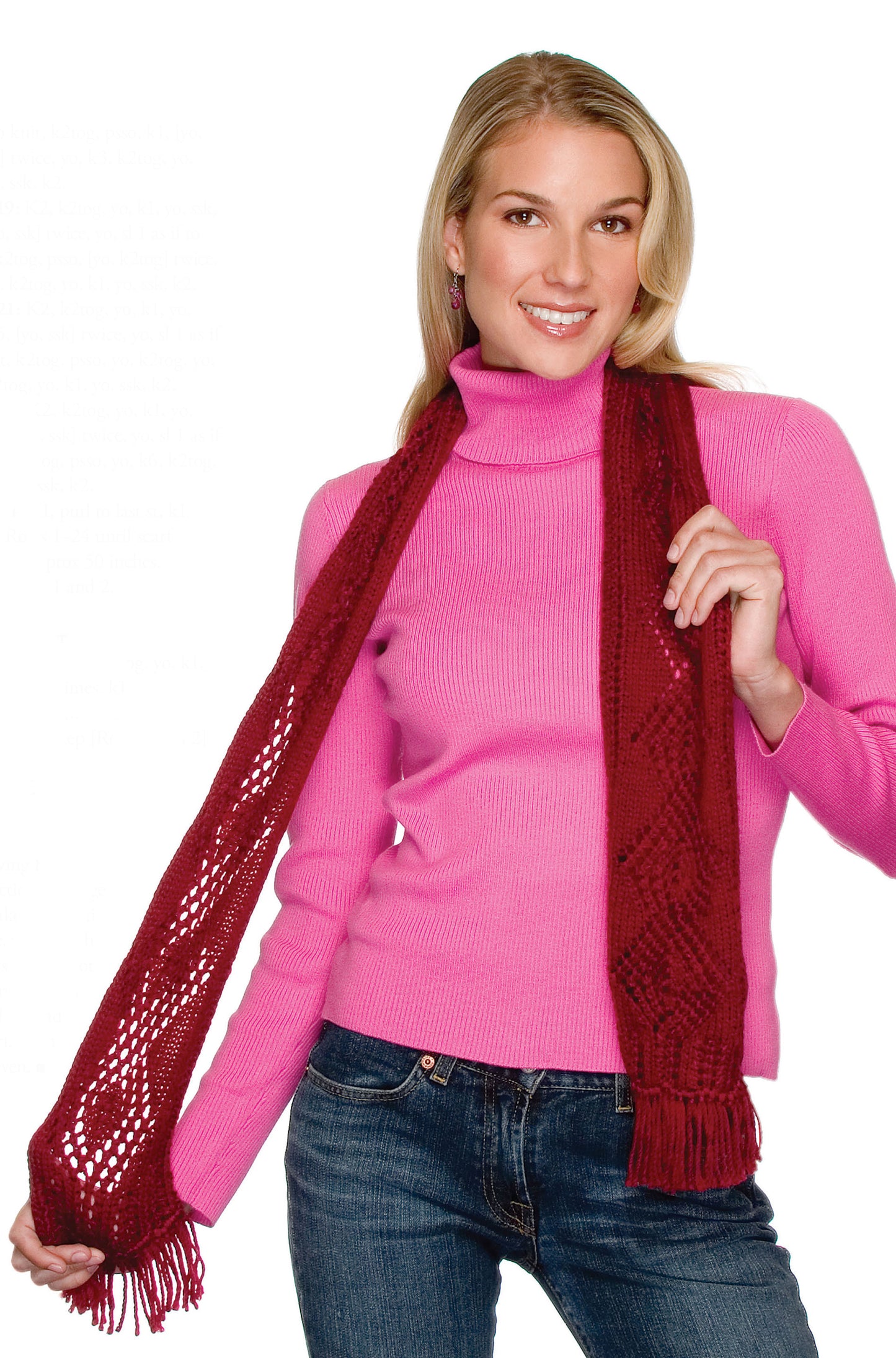 A smiling woman with long blonde hair poses in a pink turtleneck, blue jeans, and red knit scarf against a white background—perfect inspiration for projects from Leisure Arts’ Big Book of Knit Hats & Scarves for Everyone.