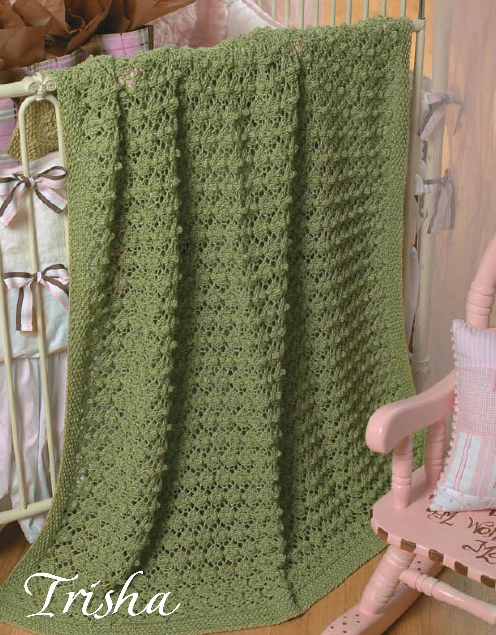 A green crocheted blanket from Leisure Arts' Quick Knit Keepsakes, Book 2, hangs on the crib. "Trisha" is stitched in white cursive in one corner. A pink rocking chair and a pillow sit nearby.