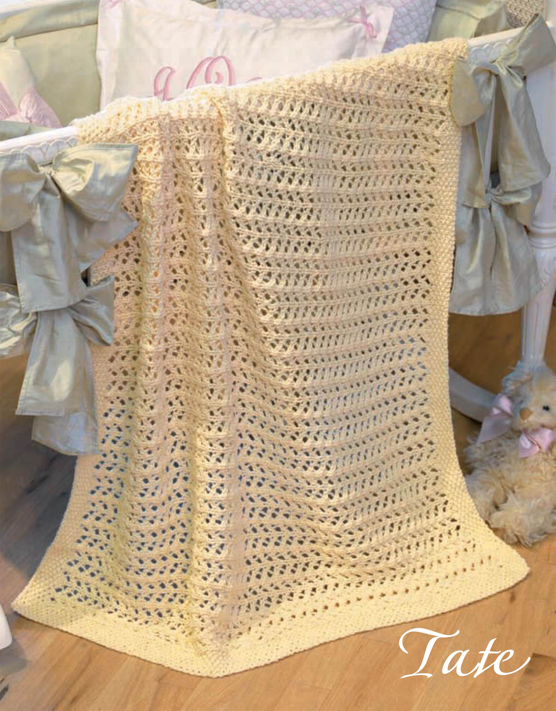 Quick Knit Keepsakes, Book 2 by Leisure Arts features a pale yellow knit baby blanket draped over a crib with satin bows. A plush teddy bear sits nearby, and "Tate" is written in script in the bottom right corner.