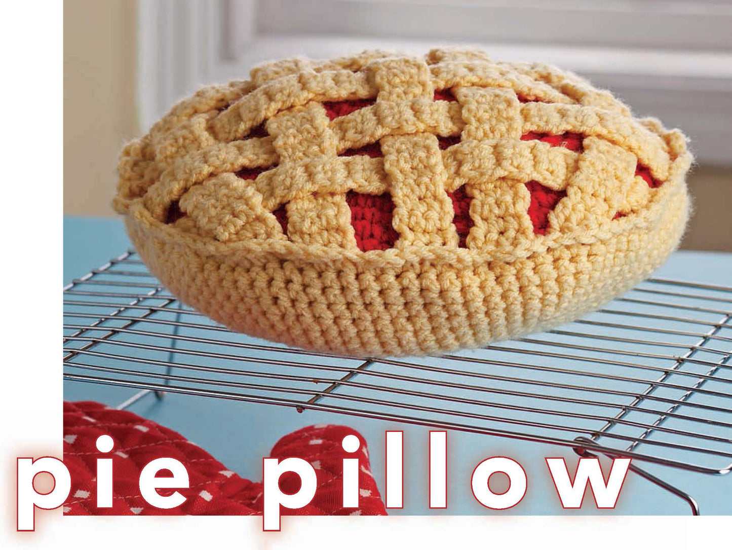 A whimsical pillow from Leisure Arts, Crochet Your Cares Away, resembles a lattice pie and sits on a metal rack. Made with worsted yarn, it's ideal for playful crochet fans. “Pie pillow” is displayed in large text at the image bottom.