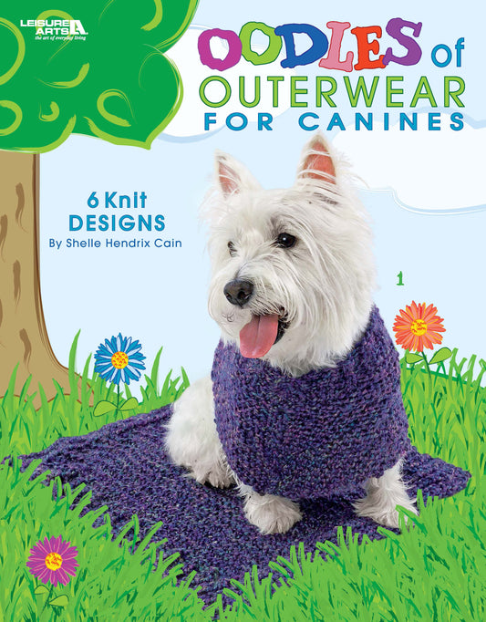 A small white dog in a purple knit scarf sits on grass with flowers. Text: Oodles of Outerwear for Canines by Leisure Arts—6 knit designs for dogs. The background shows trees and a blue sky.