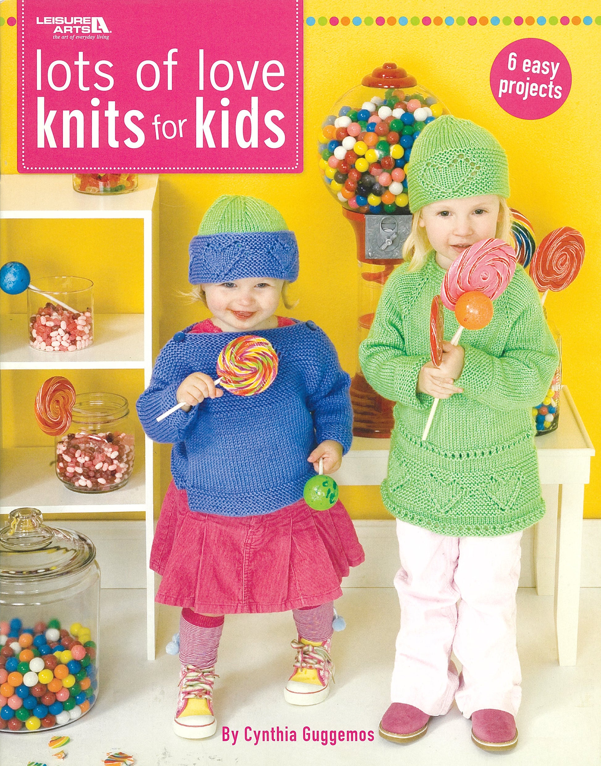 Two kids in colorful worsted yarn outfits hold big lollipops by candy jars on a yellow background with sweets. Text: Lots of Love Knits for Kids, 6 easy projects by Cynthia Guggemos. Brand: Leisure Arts.