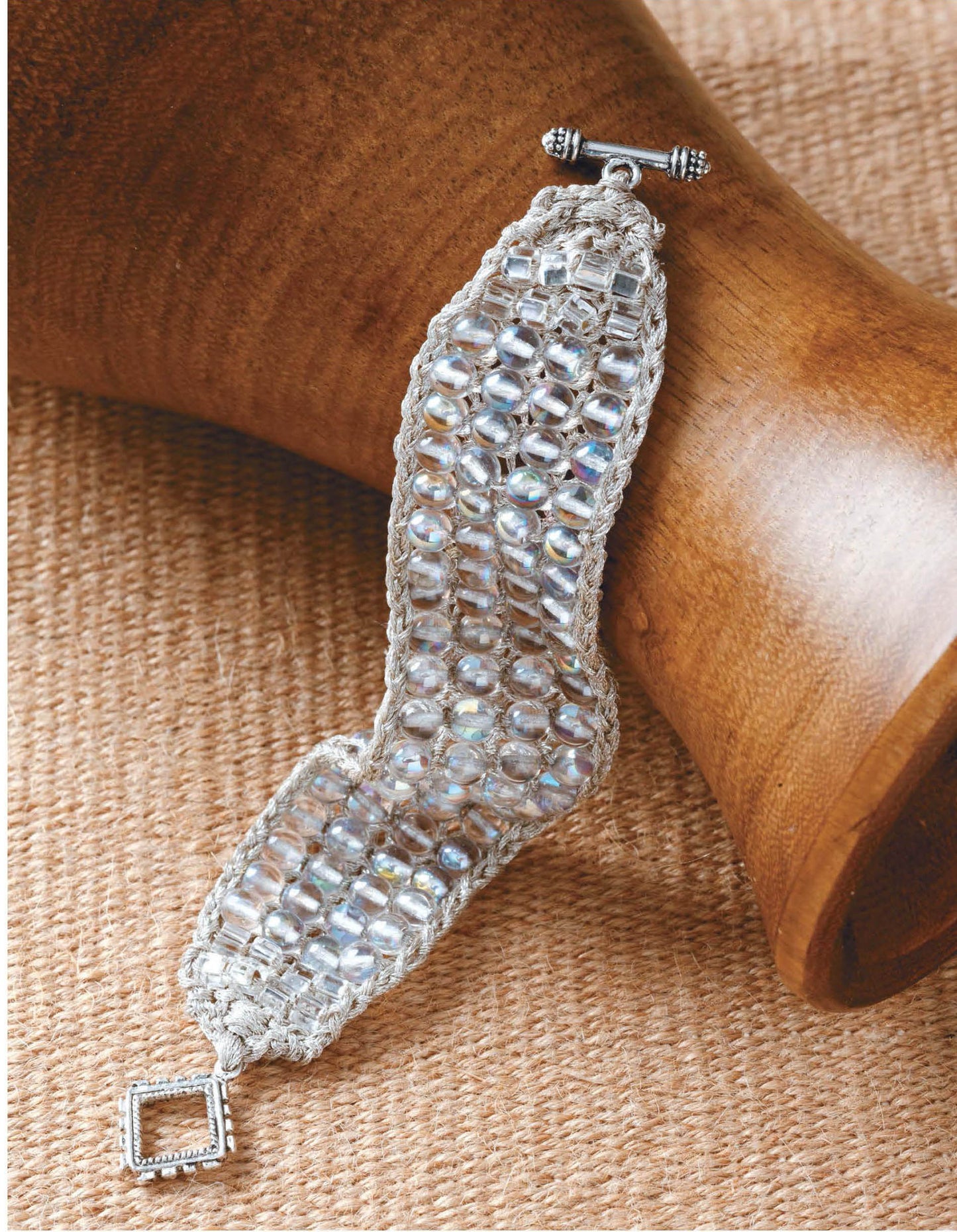 Beaded Bracelets to Knit" by Leisure Arts is displayed on burlap, showcasing a silver-toned, woven bracelet with sparkling beads—a perfect inspiration for beginners and those interested in knitted bracelet patterns.