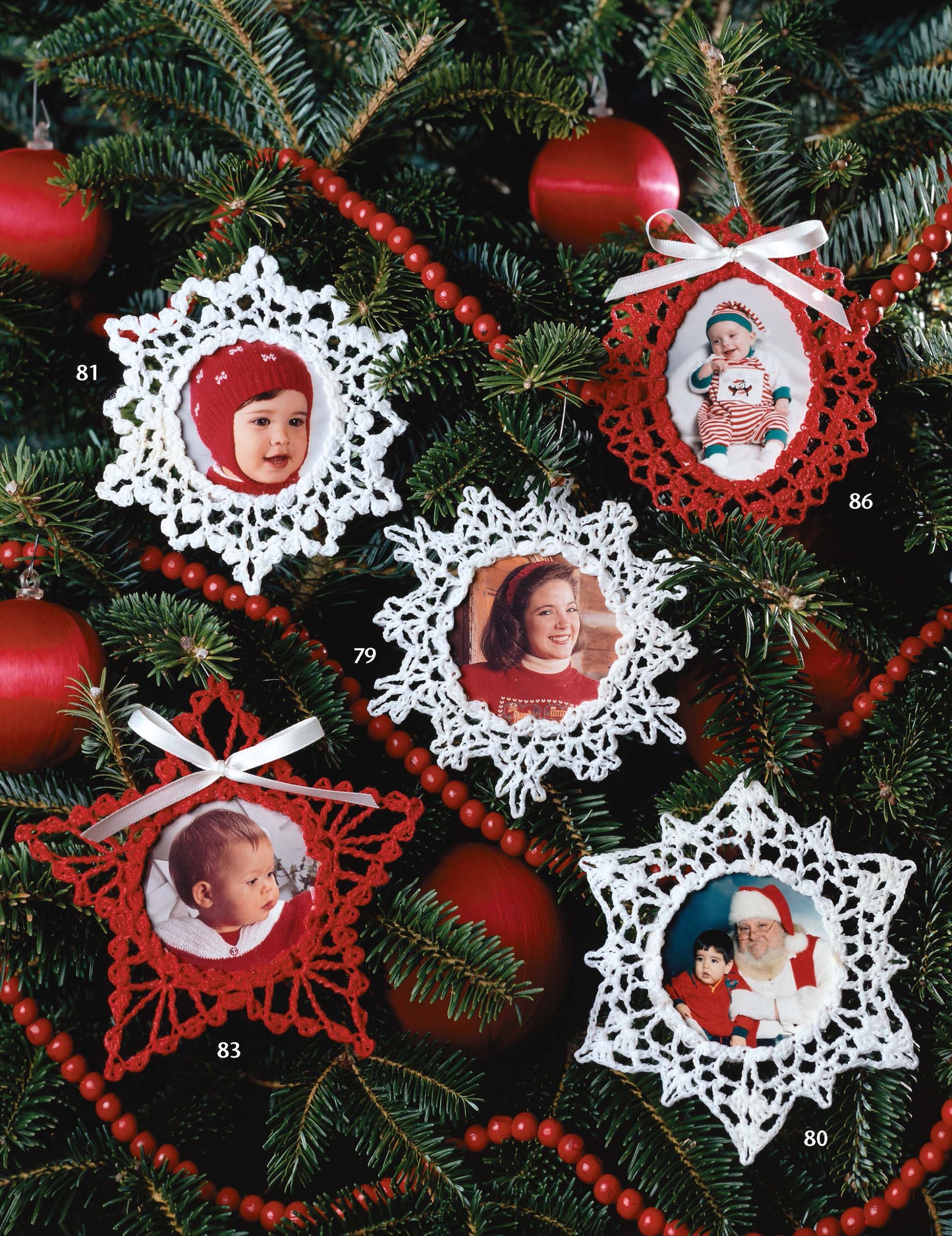 Four crochet photo ornaments from the Leisure Arts Big Book of Thread Ornaments, featuring portraits of children and Santa, hang on a tree with red baubles. These white and red ornaments have ribbon accents for a festive look.