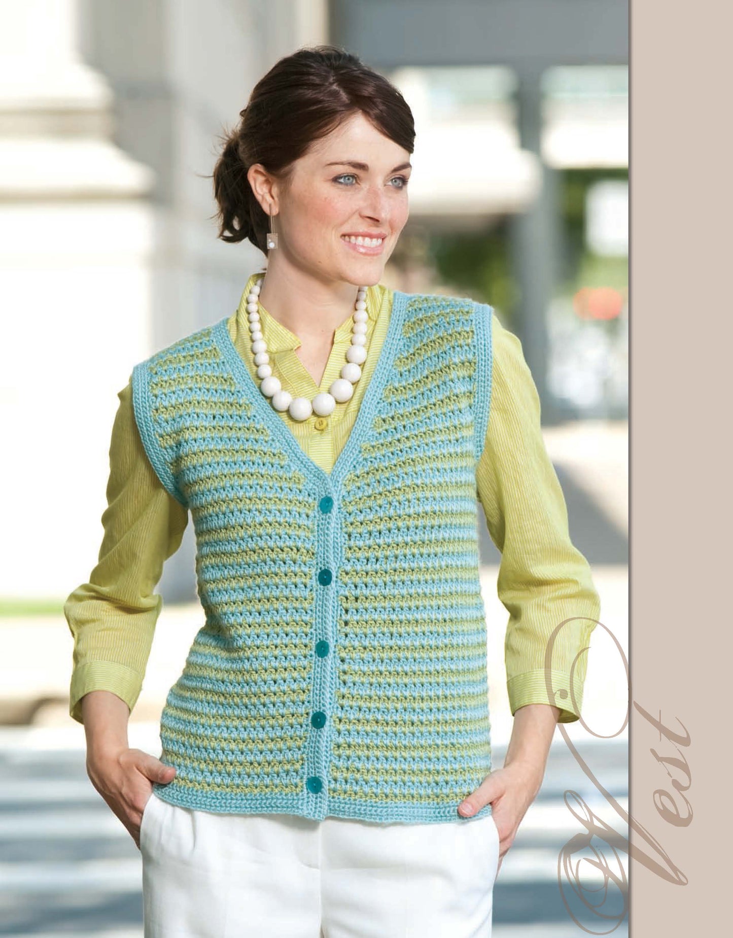 A woman in a light green blouse and blue-green crocheted vest smiles outdoors, modeling crochet fashion from "The Crochet Closet" by Leisure Arts. She wears a chunky white necklace with her hands in her pockets; “Vest” appears stylishly at the side.