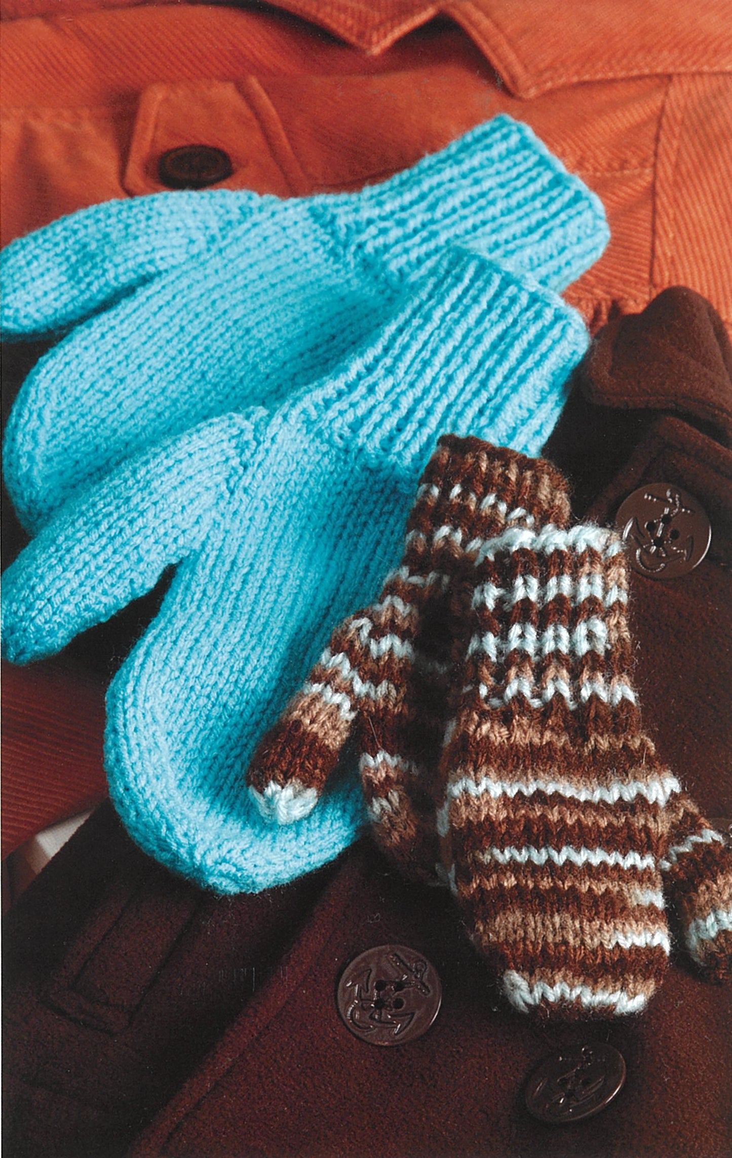Two pairs of knitted mittens—a large light blue and a small striped—rest on brown and orange coats with big buttons, evoking Leisure Arts' “Knit Along with Debbie Macomber—A Charity Guide for Knitters.”.