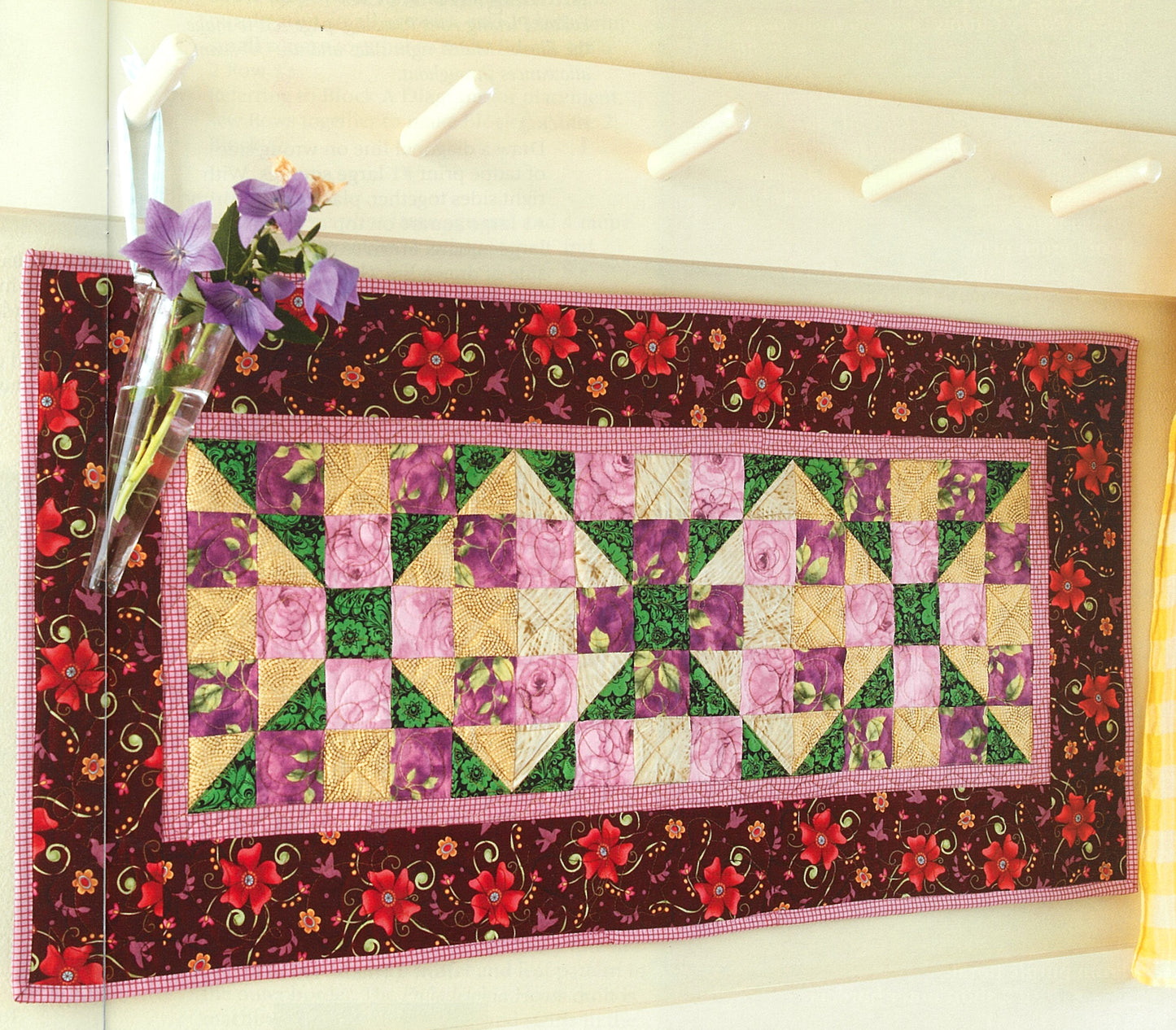 Pat Sloan's Camera, Color, Quilts! by Leisure Arts features a vibrant quilted table runner with geometric patchwork in purple, pink, green, and yellow, accented by a floral border and complemented with decorative touches.