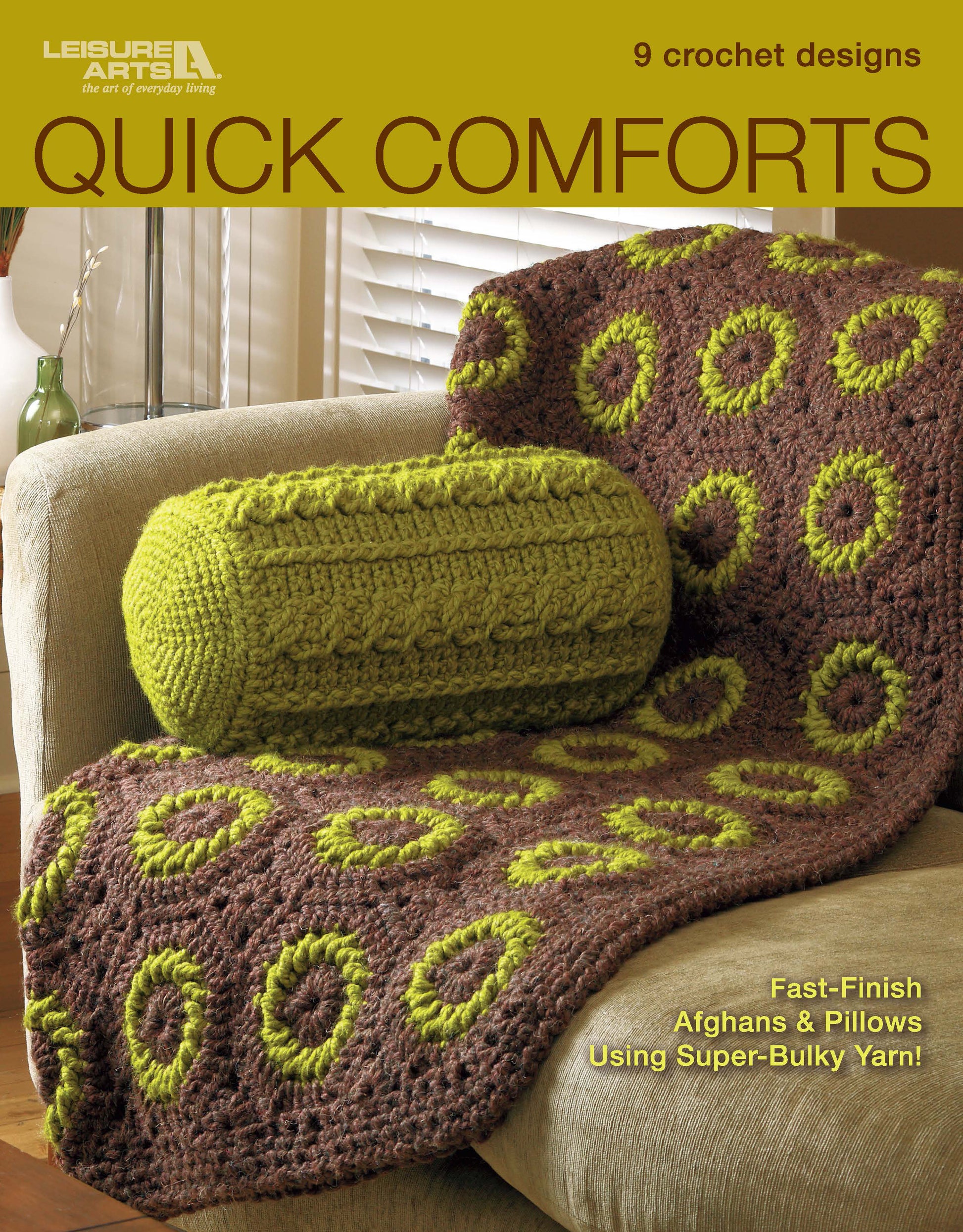 A brown afghan with green circles and a matching green crochet pillow, made with super bulky yarn, are on a beige armchair. Featured on the cover of Leisure Arts' crochet pattern book Quick Comforts Home Makeover.