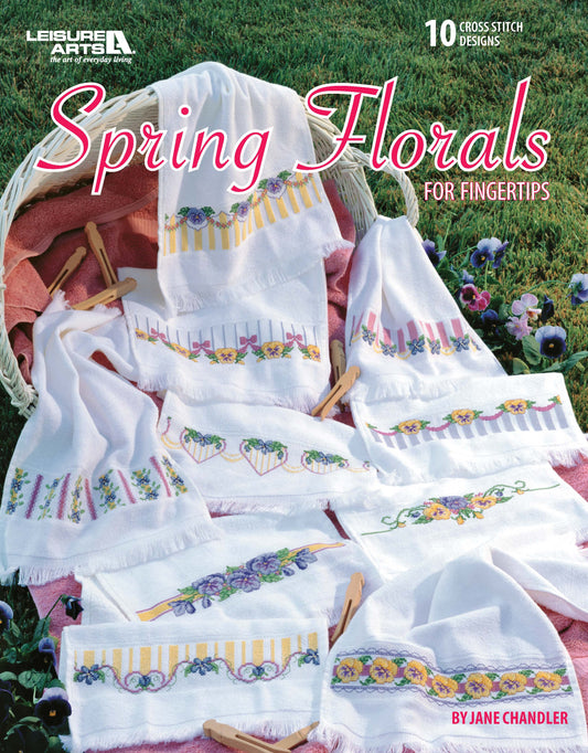 Leisure Arts' "Spring Florals For Fingertips" showcases white towels with bright floral patterns and cross stitch designs displayed in a basket—an elegant home decor accent.