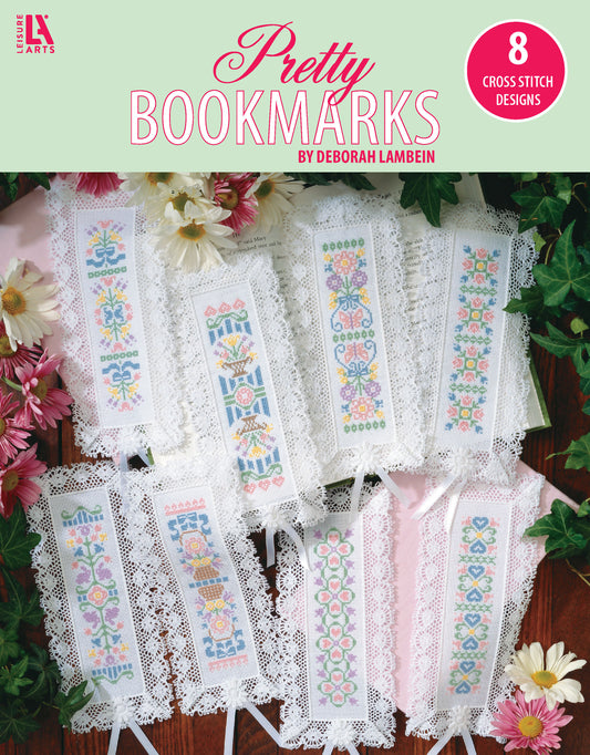 A set of 8 lace-edged bookmarks stitched with embroidery floss on 18-count aida, featuring pastel floral and geometric designs. Displayed on white cloth with pink and yellow flowers. Cross Stitch Pretty Bookmarks by Leisure Arts.