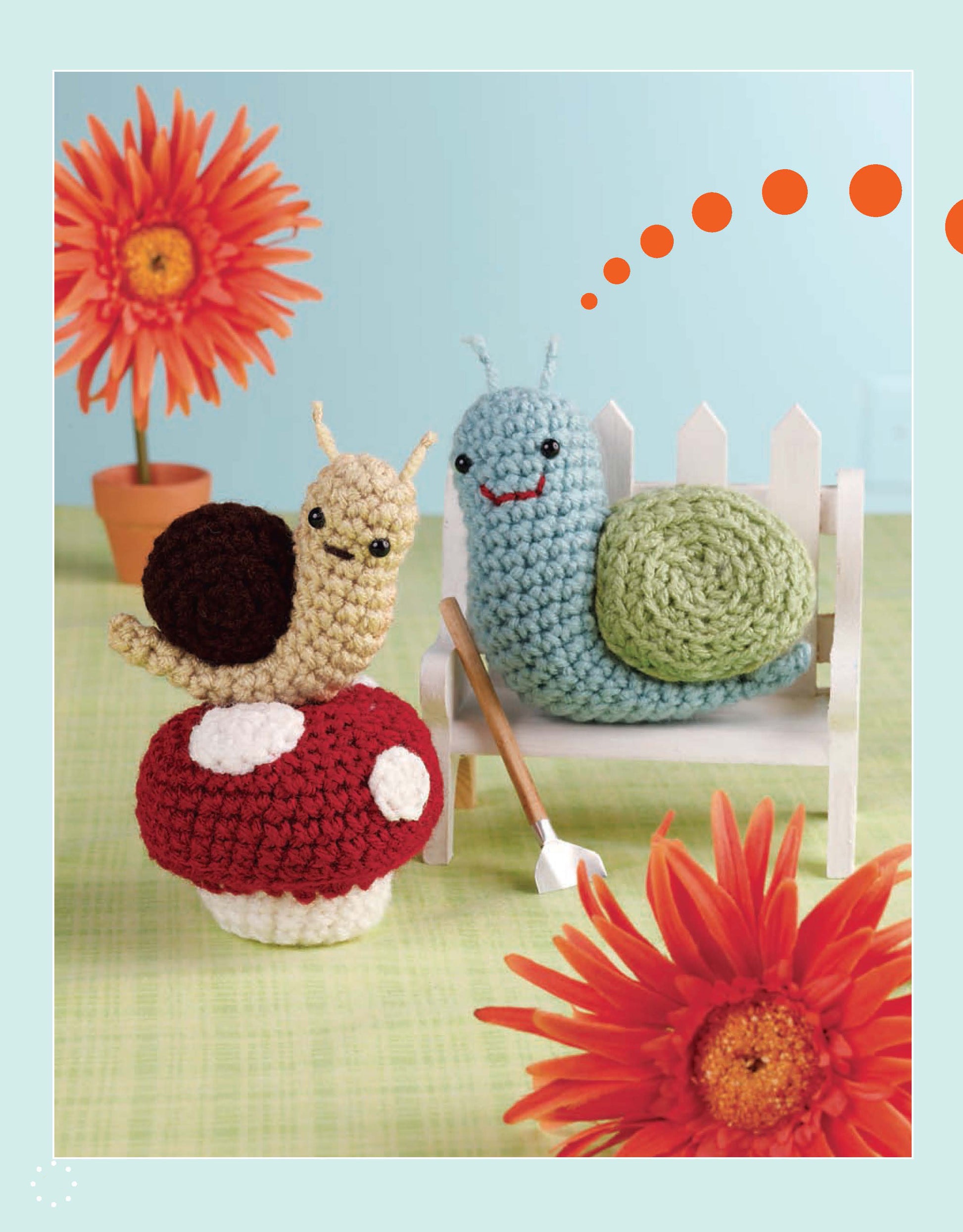 From Leisure Arts’ “More Cute Little Animals To Crochet”: two adorable crocheted animals—a green and blue snail on a white bench and a cream and brown one on a red mushroom—surrounded by orange flowers, ideal for beginner crafters.