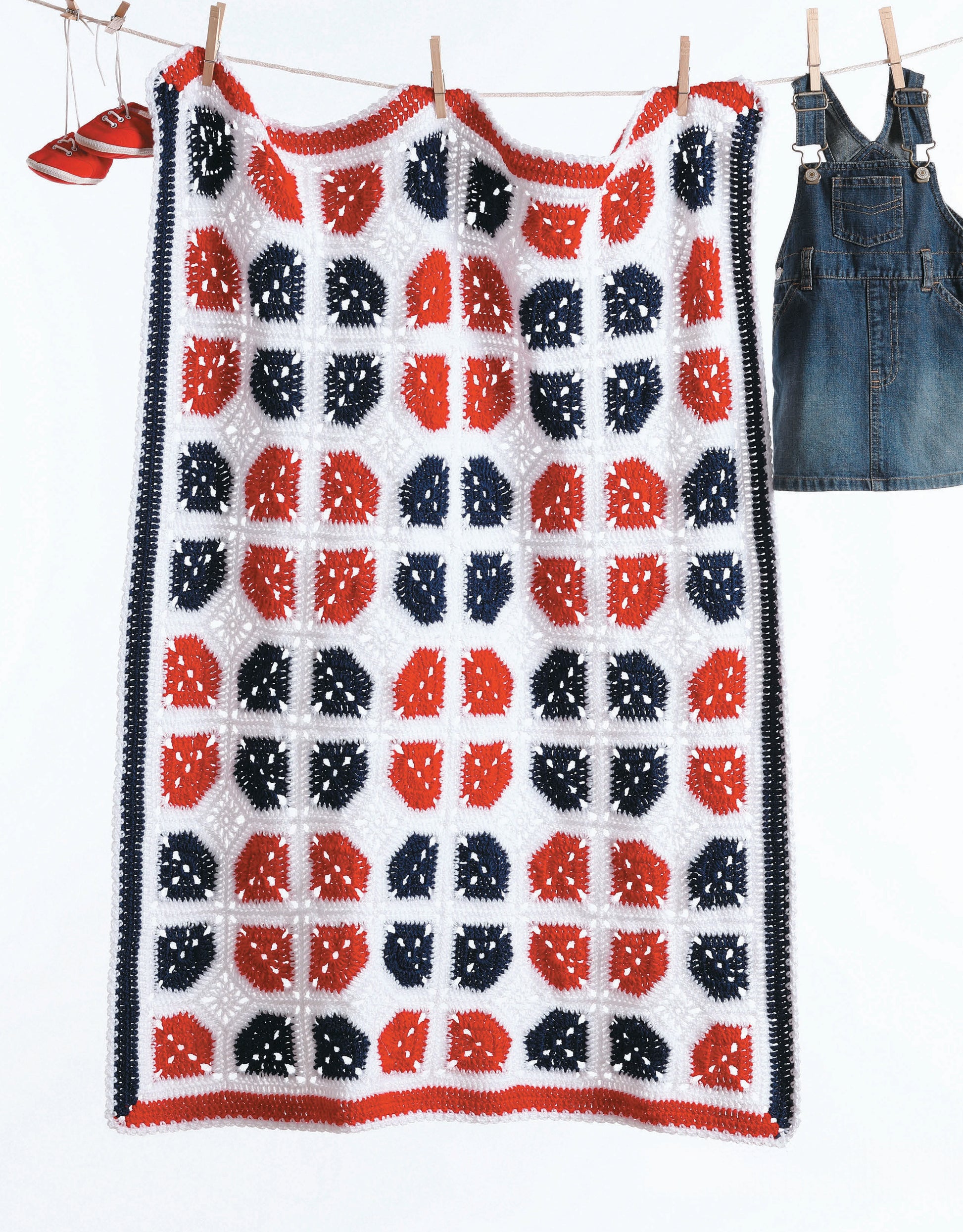 The "A Year of Baby Afghans, Book 5" by Leisure Arts features a crocheted blanket with vibrant red, white, and blue squares, shown hanging on a clothesline between denim overalls and a single red shoe.