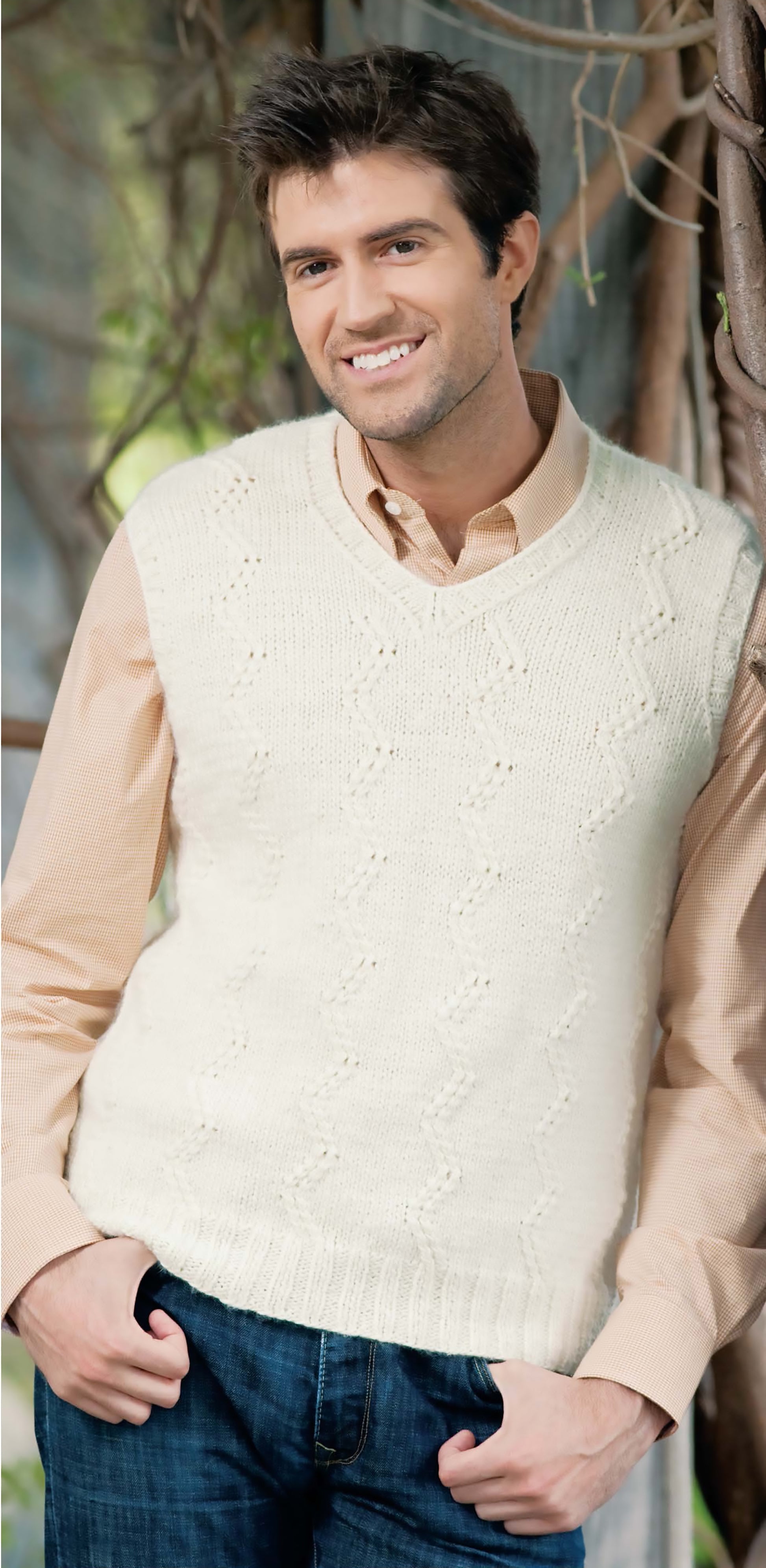 A smiling man in a light beige shirt and cream textured sweater vest showcases a project from the Blossom Street Collection Book 2 digital download by Leisure Arts, ideal for easy knitting or step-by-step instructions.