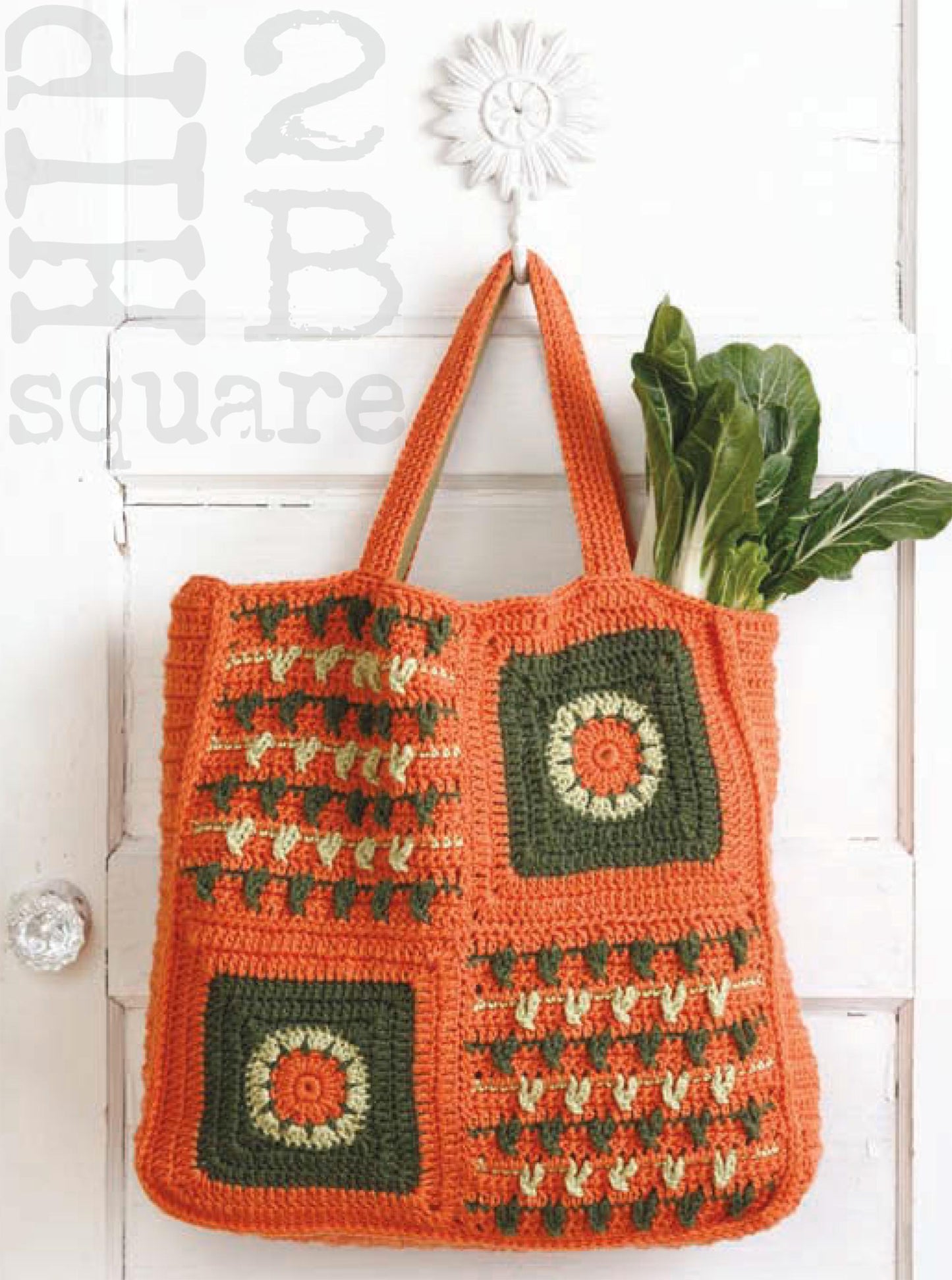 An orange crocheted tote with green and yellow square motifs from Leisure Arts’ Hip 2 B Square Totes & Bags Digital Download hangs on a white door hook, leafy greens inside. The phrase “2 B square” is visible in the background.