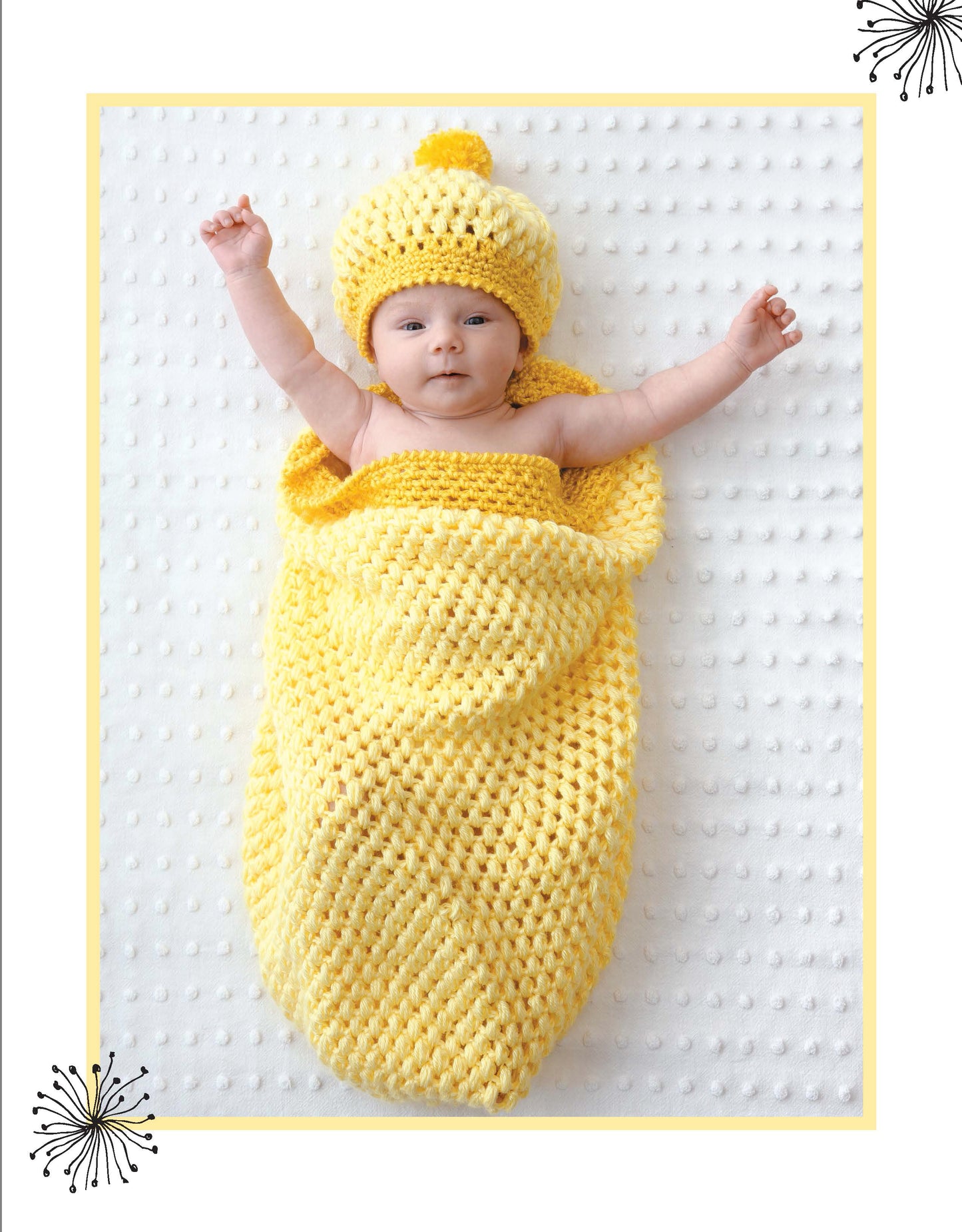 A baby rests on a white blanket, wrapped in a Crochet Dreamy Cocoons sack and cap by Leisure Arts, arms outstretched. Black starbursts accent two corners, showcasing these adorable crochet patterns.
