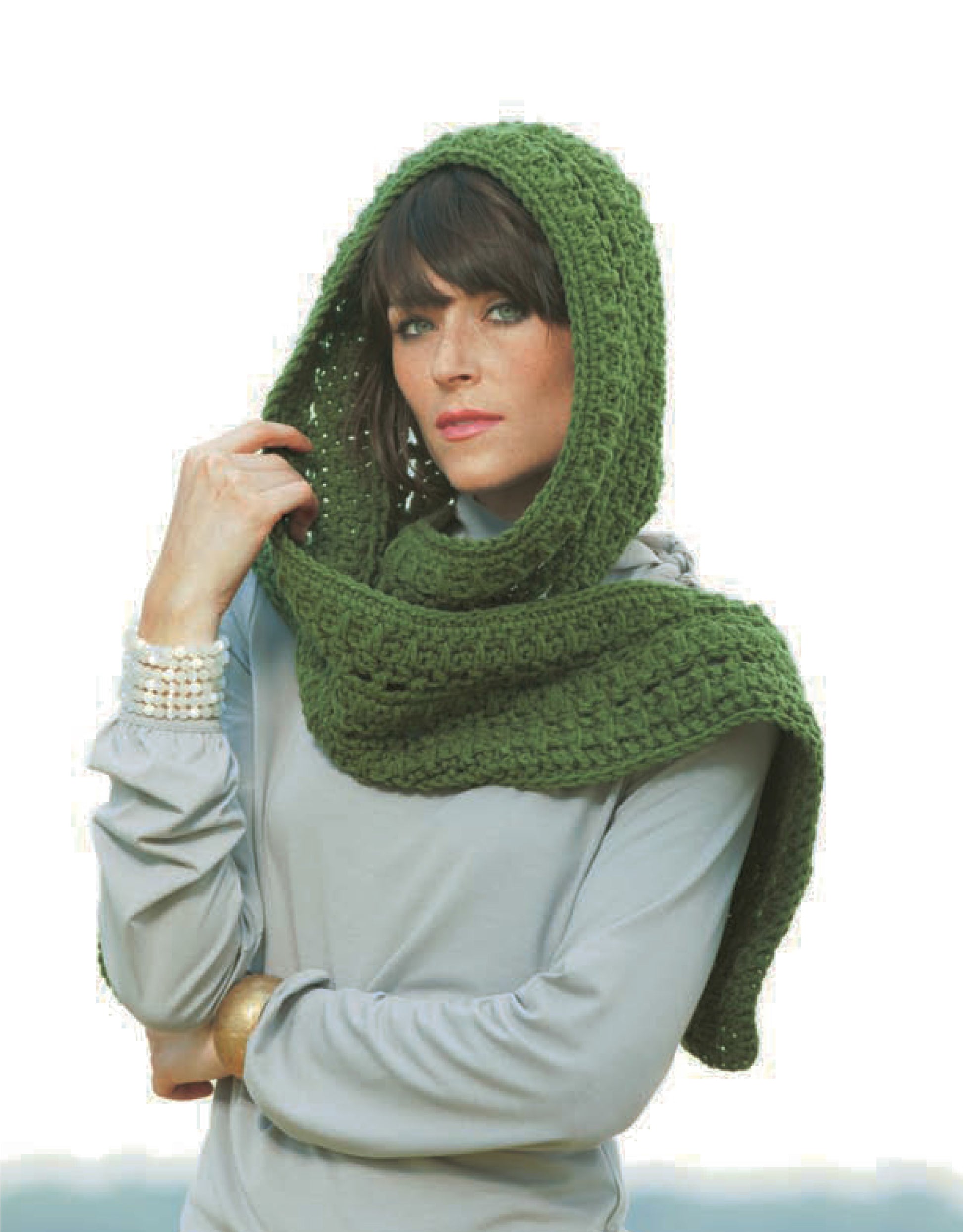A woman models a green scarf from Leisure Arts’ Hooded Scarves Digital Download, perfect for beginner crochet projects, over a light gray top with pearl bracelets and a gold bangle against a white background.