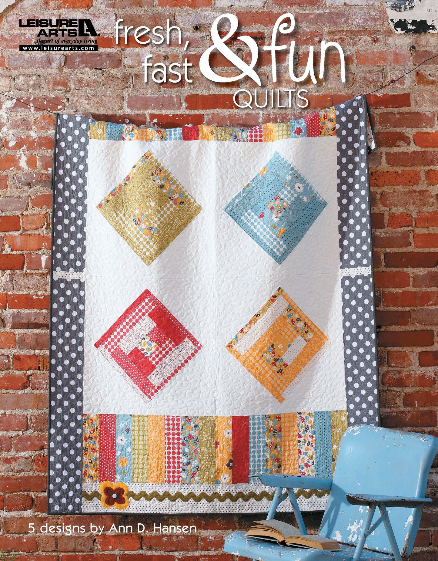 A colorful quilt hangs on a brick wall, with a blue metal chair in front. Text: Fresh, Fast & Fun Quilts by Leisure Arts—5 designs with step-by-step instructions by Ann D. Hansen.