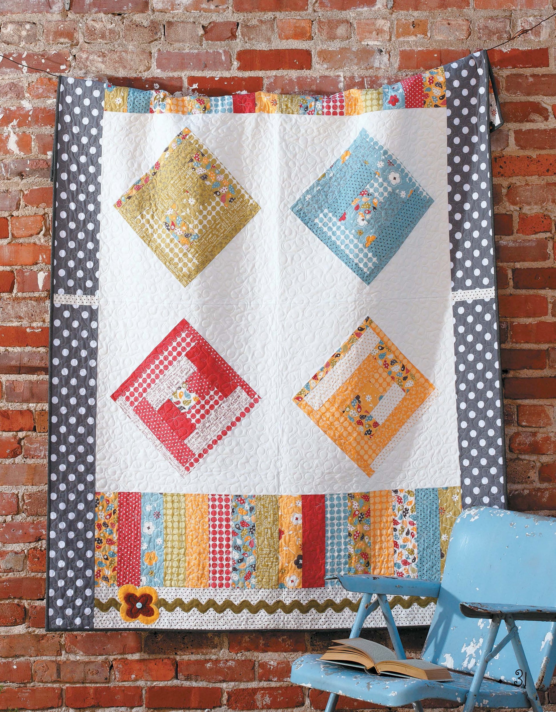 The Fresh, Fast & Fun Quilts book by Leisure Arts is displayed on a brick wall, featuring four bold diamond patchwork blocks with polka-dot borders. A blue chair with an open book sits in front, highlighting its vibrant, fat quarter friendly designs.