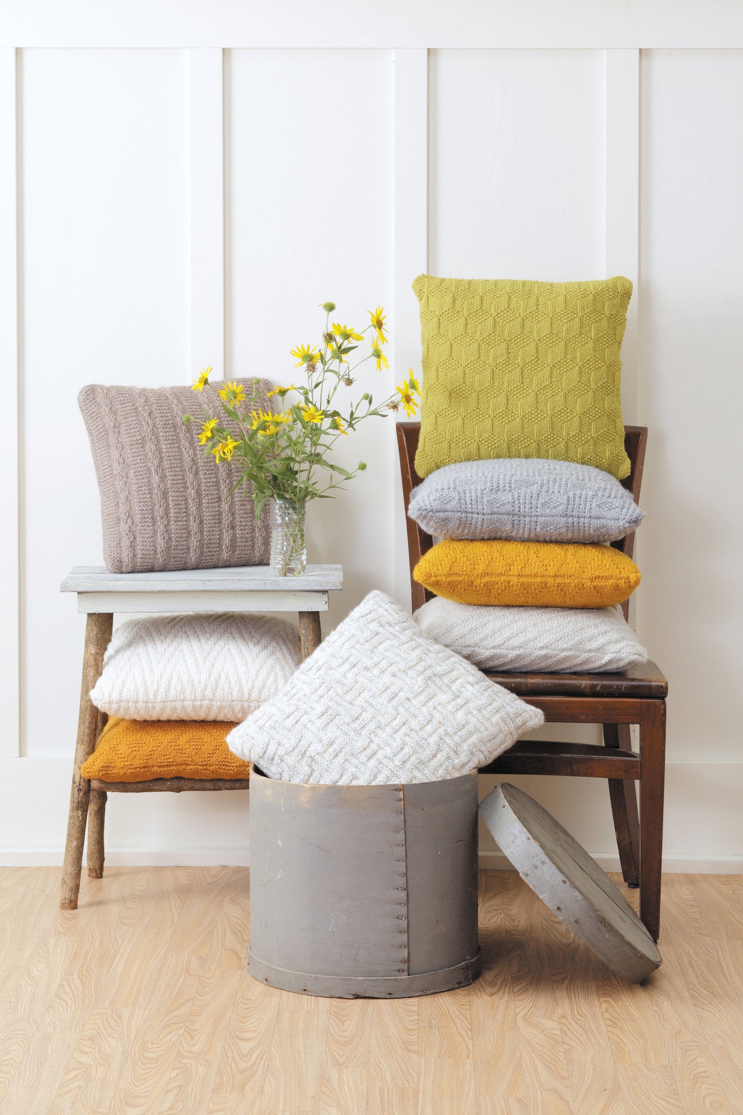 Create a cozy setting with pillows in mustard yellow, gray, and beige, crafted from textured stitch patterns found in the Easy Textured Knits Digital Download by Leisure Arts—perfect on chairs or next to rustic decor.