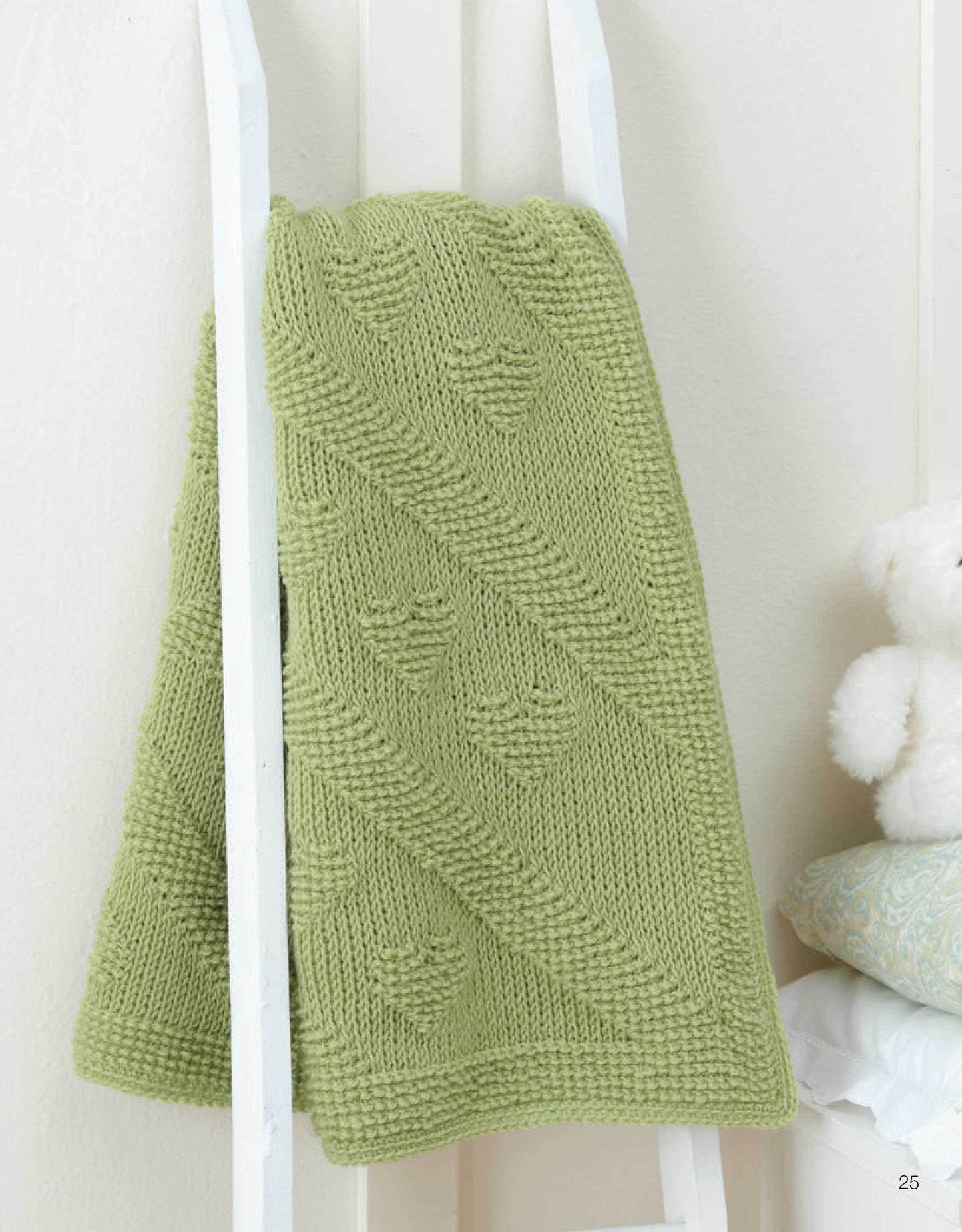 The "Ultimate Beginner's Guide to Tunisian Crochet" by Leisure Arts is displayed on a white ladder, with cozy bedding and a teddy bear in the background—perfect for anyone starting their crochet journey.