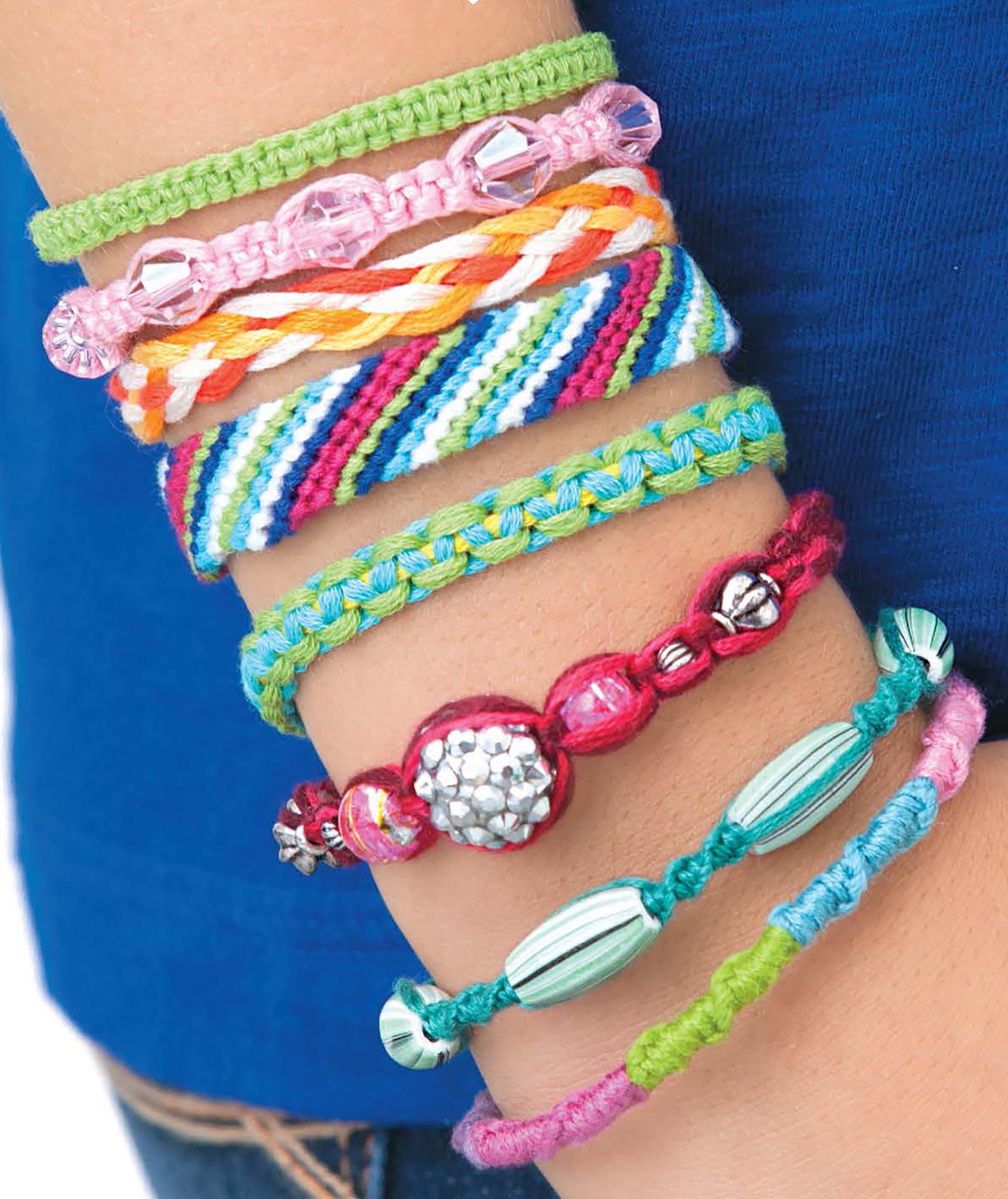 A close-up shows a wrist adorned with colorful, braided and beaded bracelets, set against a blue shirt—ideal inspiration for crafters or kids exploring the "Friendship Bracelets Digital Download" from Leisure Arts.