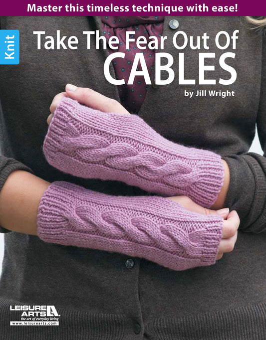 Wearing hand-knitted, light purple fingerless gloves with a cable pattern. Text: Take the Fear Out of Cables Knitting by Leisure Arts—your essential guide to mastering beginner cable knitting patterns with confidence!.