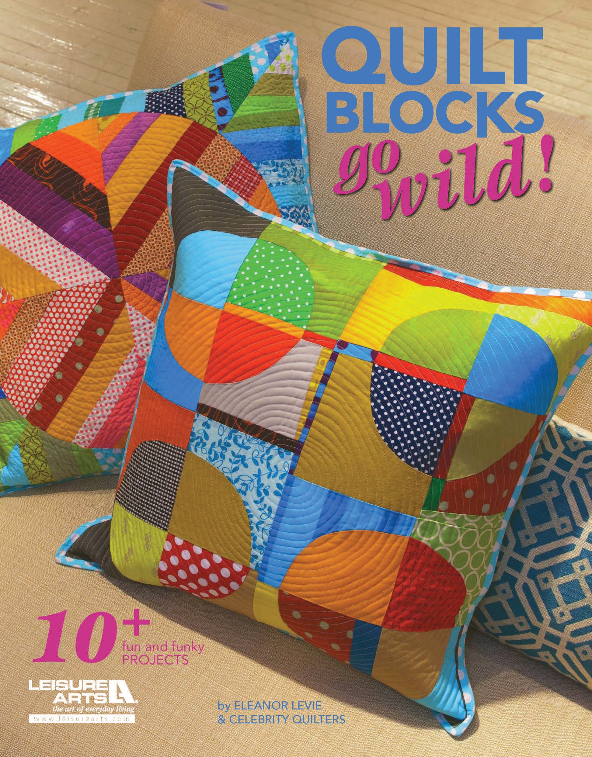 Colorful quilt block pillows are stacked on a beige surface. The Leisure Arts magazine “Quilt Blocks Go Wild!” features bold text, quilt patterns, and step-by-step photos—perfect for beginning quilters and fun projects.