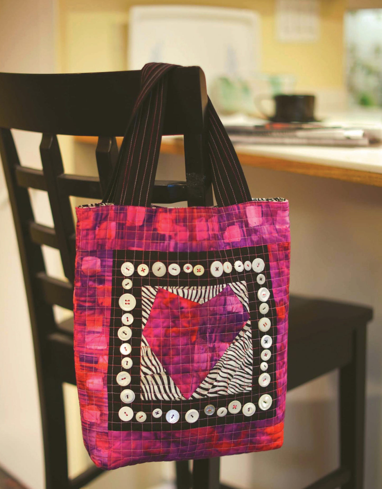 Quilt Blocks Go Wild! by Leisure Arts—a vibrant quilted tote featuring a heart motif, zebra print accents, and a white button border—hangs on a black chair in the kitchen, perfect for beginner quilters.