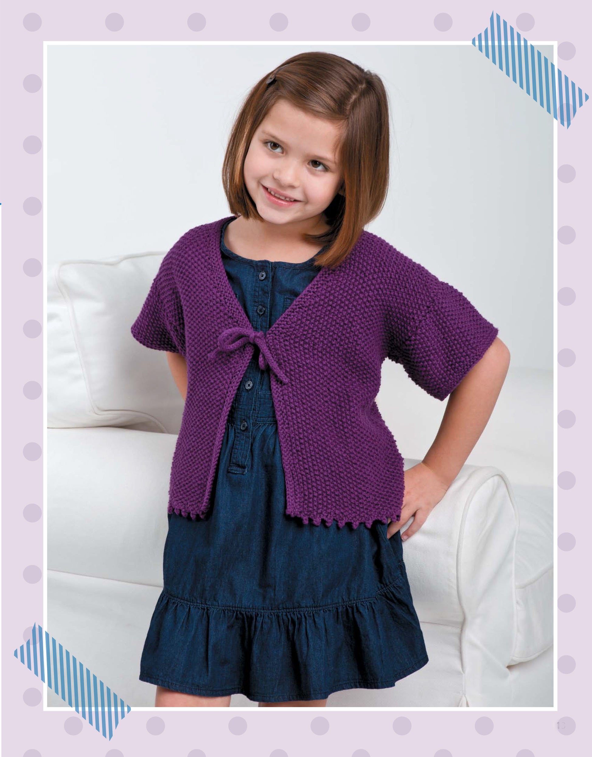 A smiling girl with a brown bob wears a blue dress and purple knit cardigan made with "Pick the Pieces Knitting" by Leisure Arts, perfect for beginners. She stands with one hand on her hip in front of a white couch, framed by polka dots.