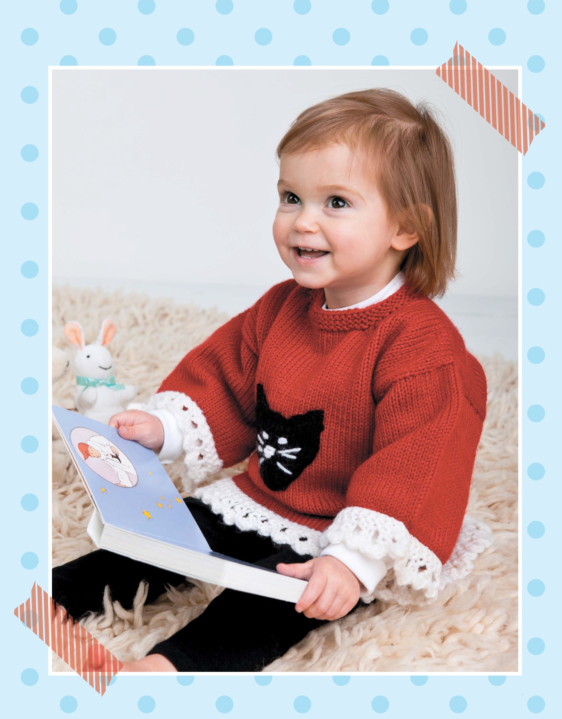 A smiling toddler with light brown hair sits on a fuzzy rug, wearing a red sweater with a black cat design. Get inspired for your next project with children's sweater knitting patterns from Pick the Pieces Knitting by Leisure Arts. A toy bunny sits nearby.