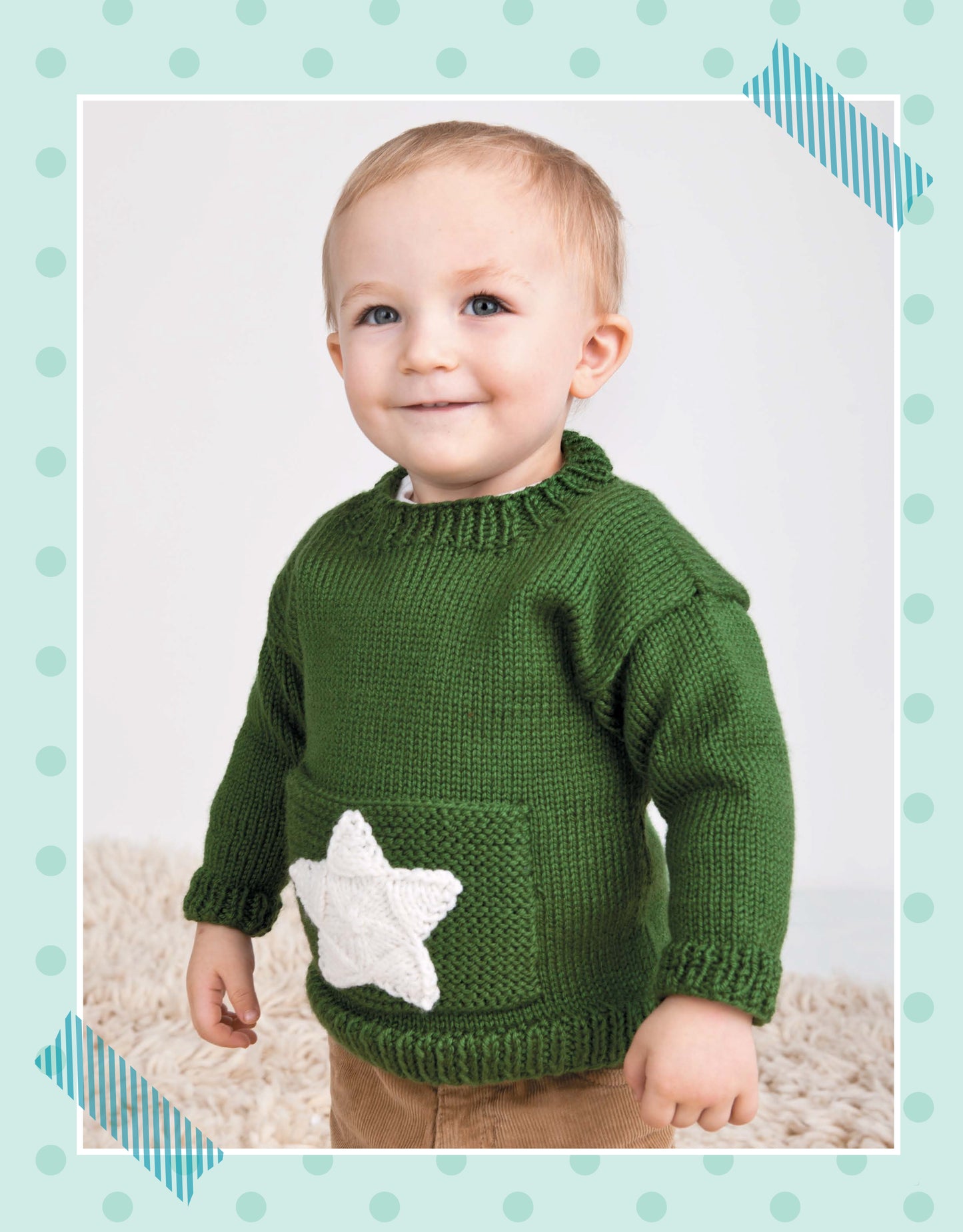 A smiling toddler indoors wears a green sweater with a white star pocket—perfect for beginner projects from Leisure Arts' Pick the Pieces Knitting. The image features a light blue polka-dot border and diagonal blue-striped tape accents.