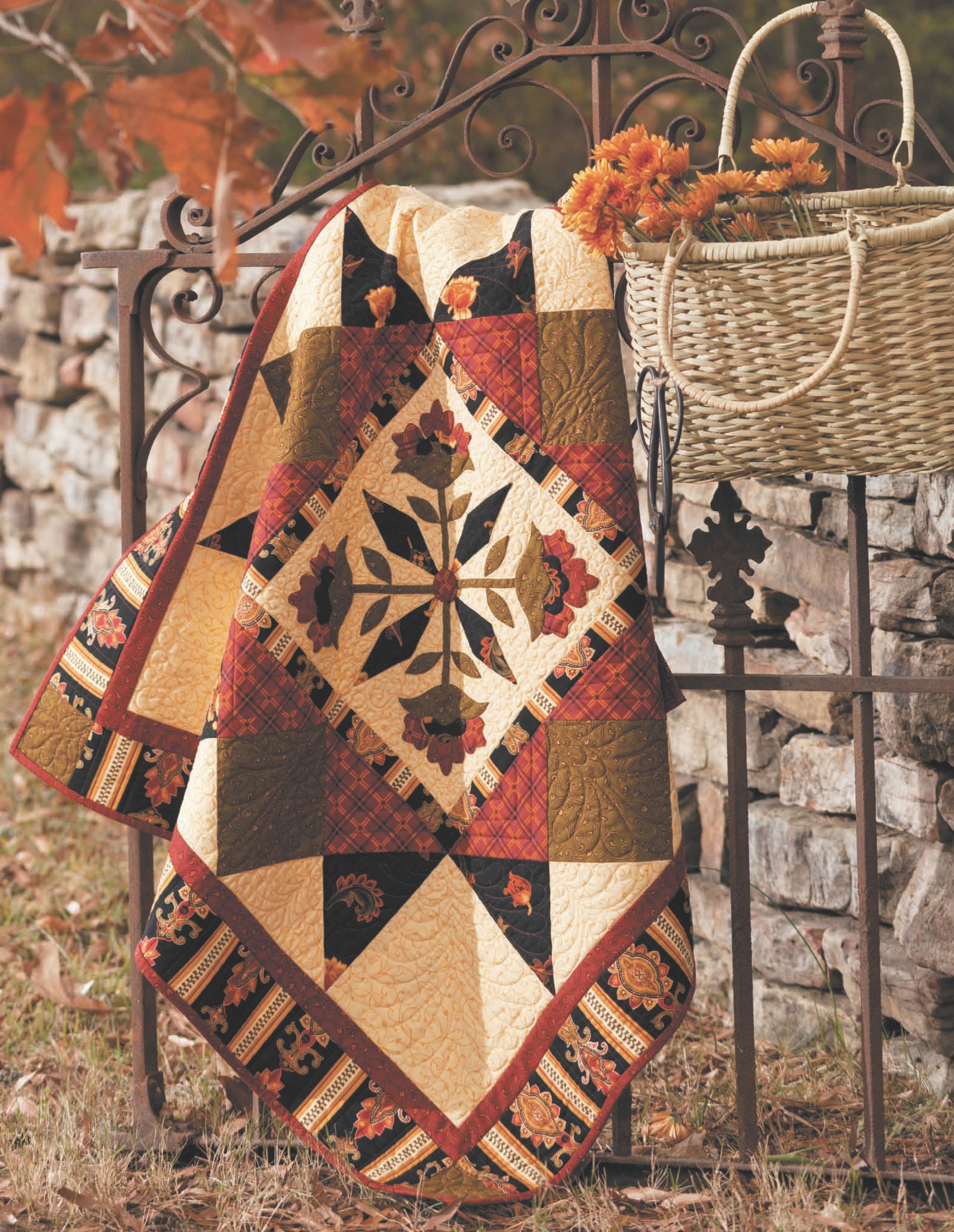 The "Quilts to Warm Today's Home" digital download by Leisure Arts features colorful autumn-toned classic quilt patterns, perfect for draping over an iron fence or pairing with baskets of orange flowers to create a cozy seasonal setting.