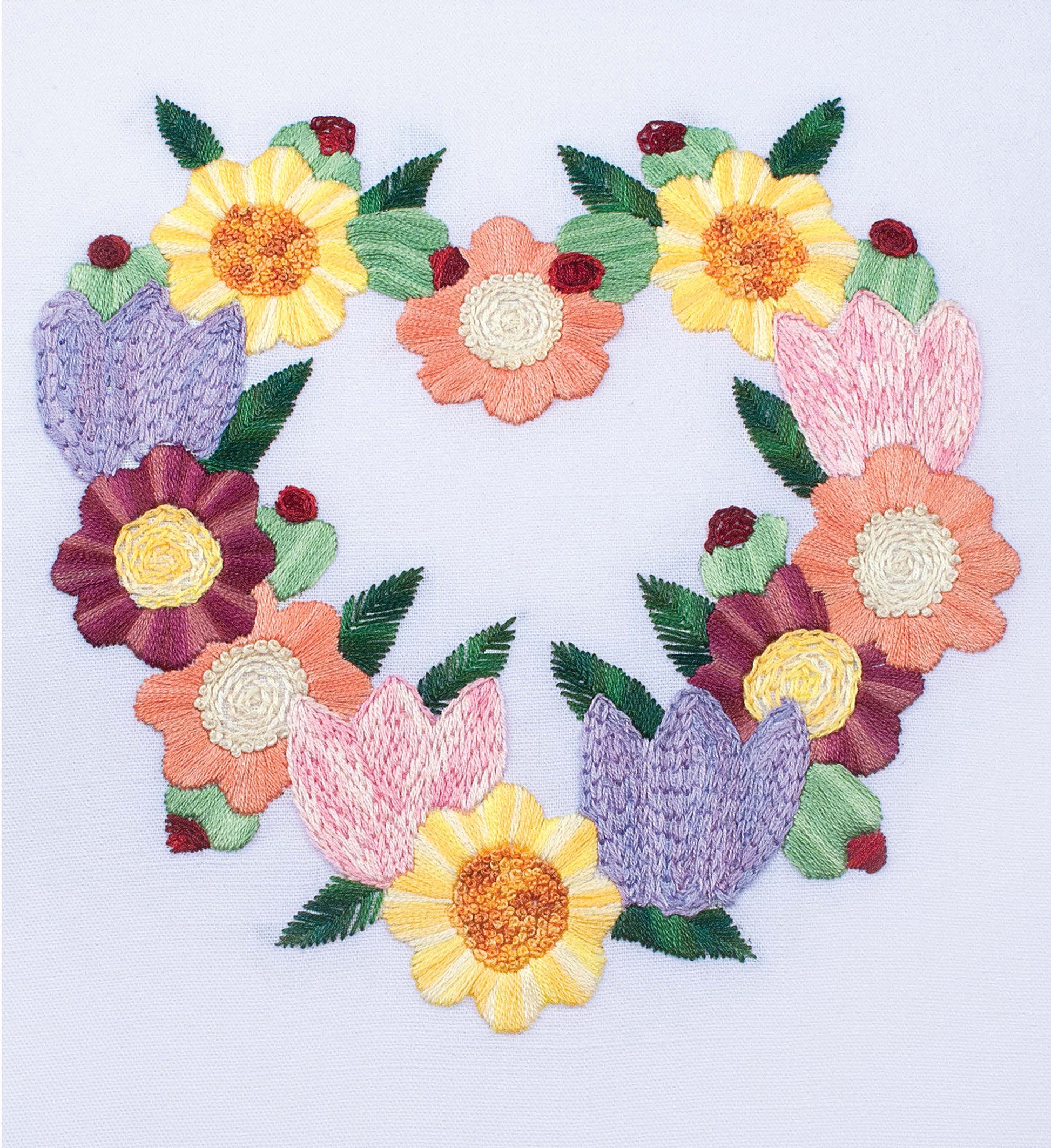 The Embroidery Stitch Guide by Leisure Arts features a heart-shaped design with yellow, pink, purple, and orange flowers on white fabric—perfect for beginners or practicing new embroidery stitches.