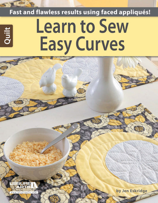 The Learn to Sew Easy Curves book from Leisure Arts features quilted placemats in yellow, gray, and white florals—ideal for beginner quilters—shown on a table set with a bowl of cereal, spoon, vase, and two white bird figurines.