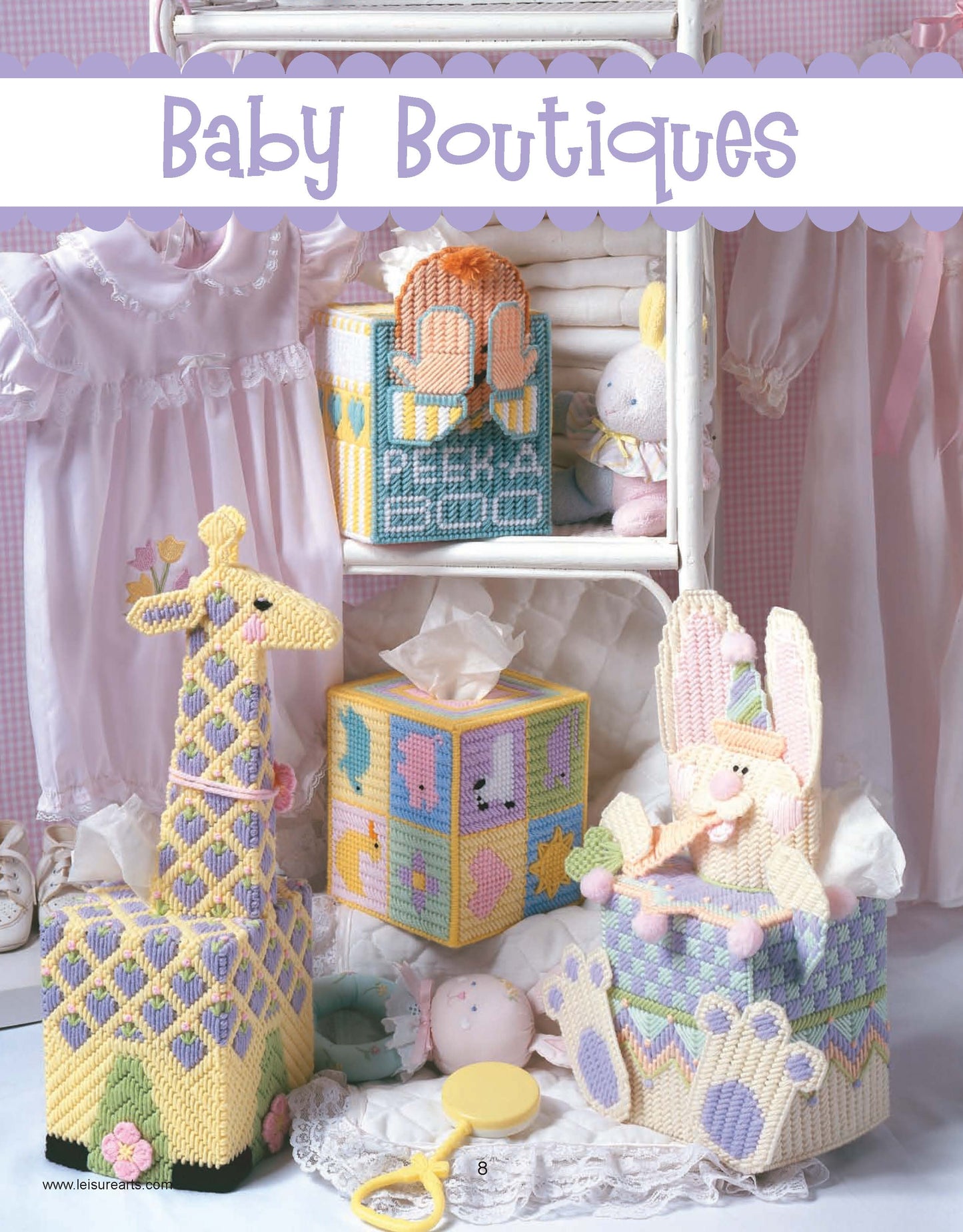 A charming display featuring Leisure Arts' "Friends for Baby in Plastic Canvas" digital download: pastel animal-themed tissue box covers, baby dresses, a rattle, and plush toys—ideal as shower favors or nursery décor.