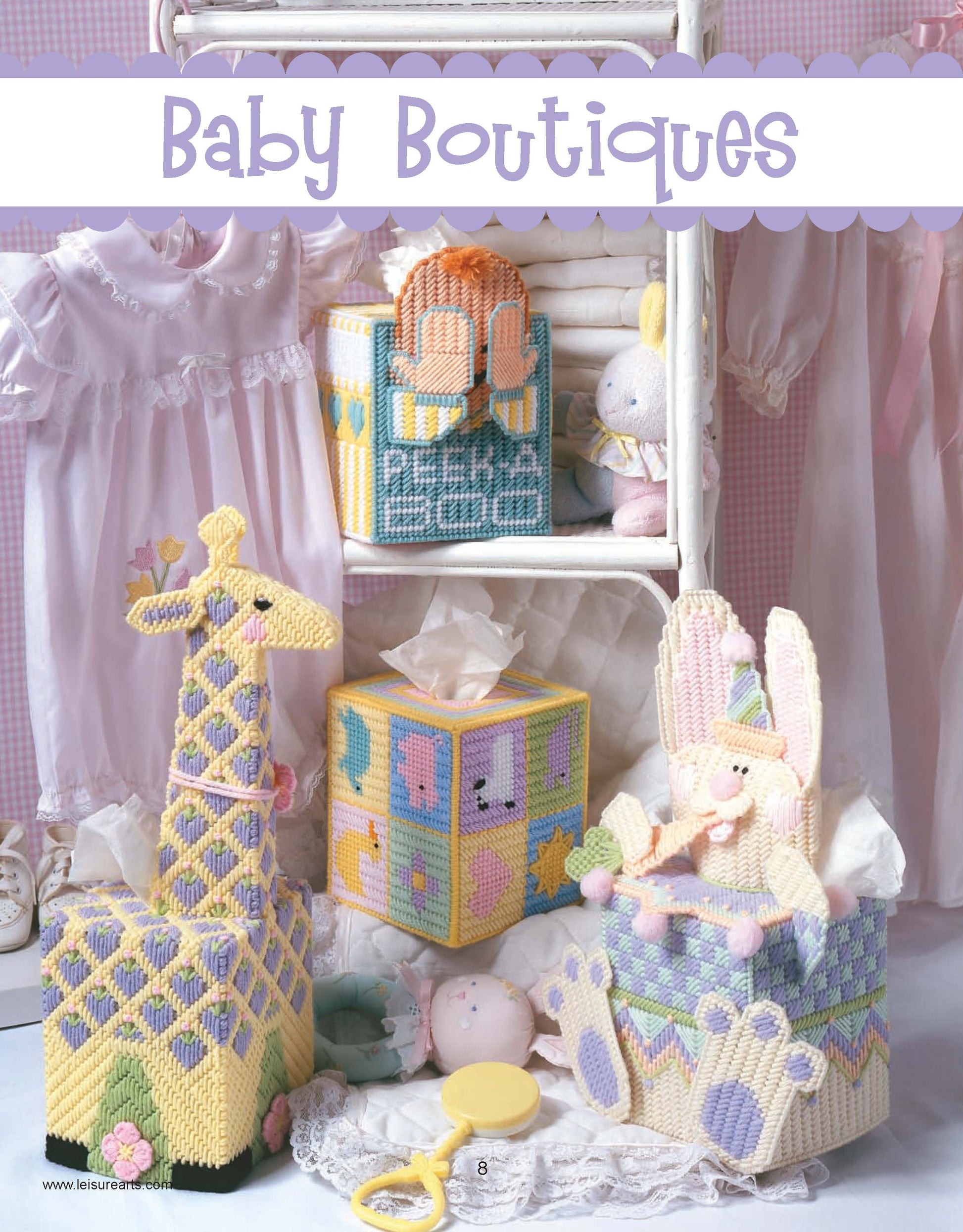 A charming display featuring Leisure Arts' "Friends for Baby in Plastic Canvas" digital download: pastel animal-themed tissue box covers, baby dresses, a rattle, and plush toys—ideal as shower favors or nursery décor.