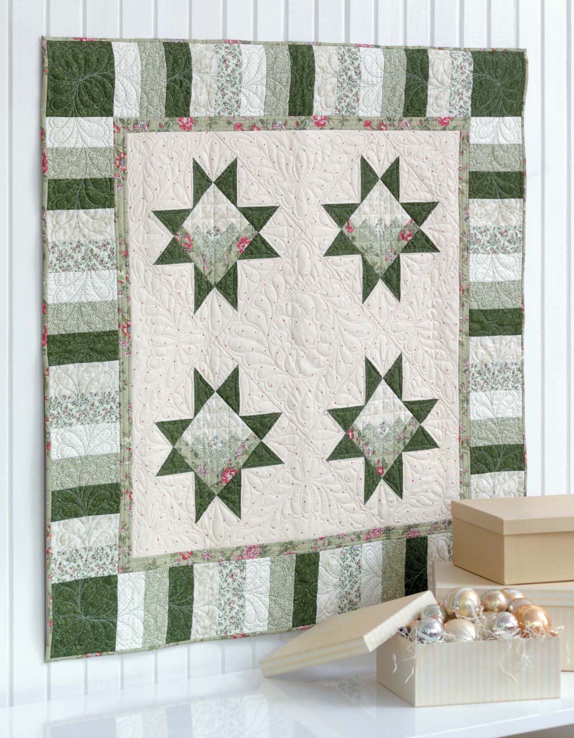 A green and cream quilt with four star patterns and a striped border hangs on a white wall, accented by Leisure Arts Christmas Sparkle—7 Whimsical Embellishments That Truly Sparkle!—for festive holiday charm.