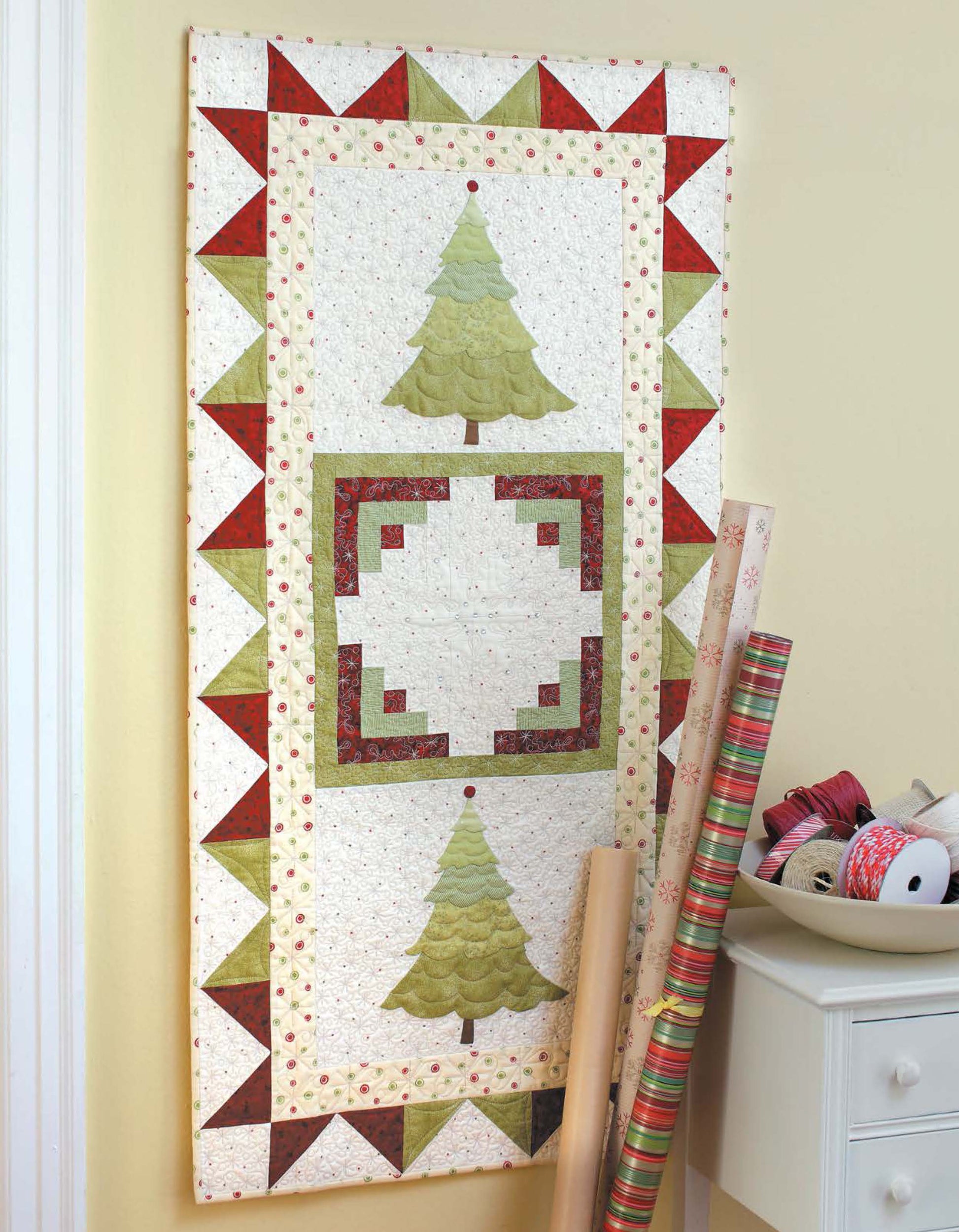 Leisure Arts’ “Christmas Sparkle—7 Whimsical Embellishments That Truly Sparkle!” adds festive cheer with sparkling designs, perfect for cozy Christmas decor alongside gift wrap and ribbons on a white cabinet against pale yellow walls.